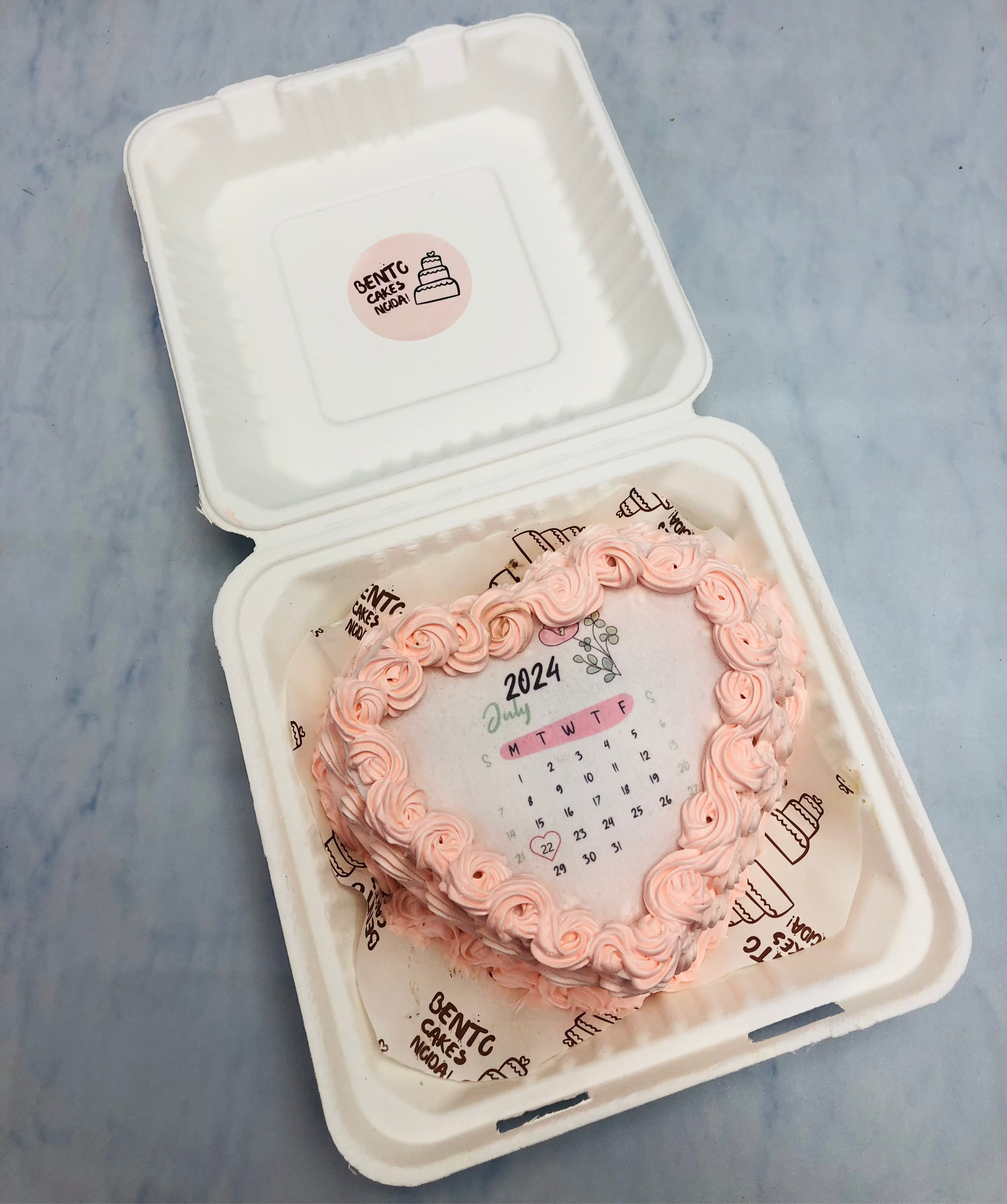 A rose pink heart shape fire bento cake with light pink truffle design on its boundary and calendar fire paper.