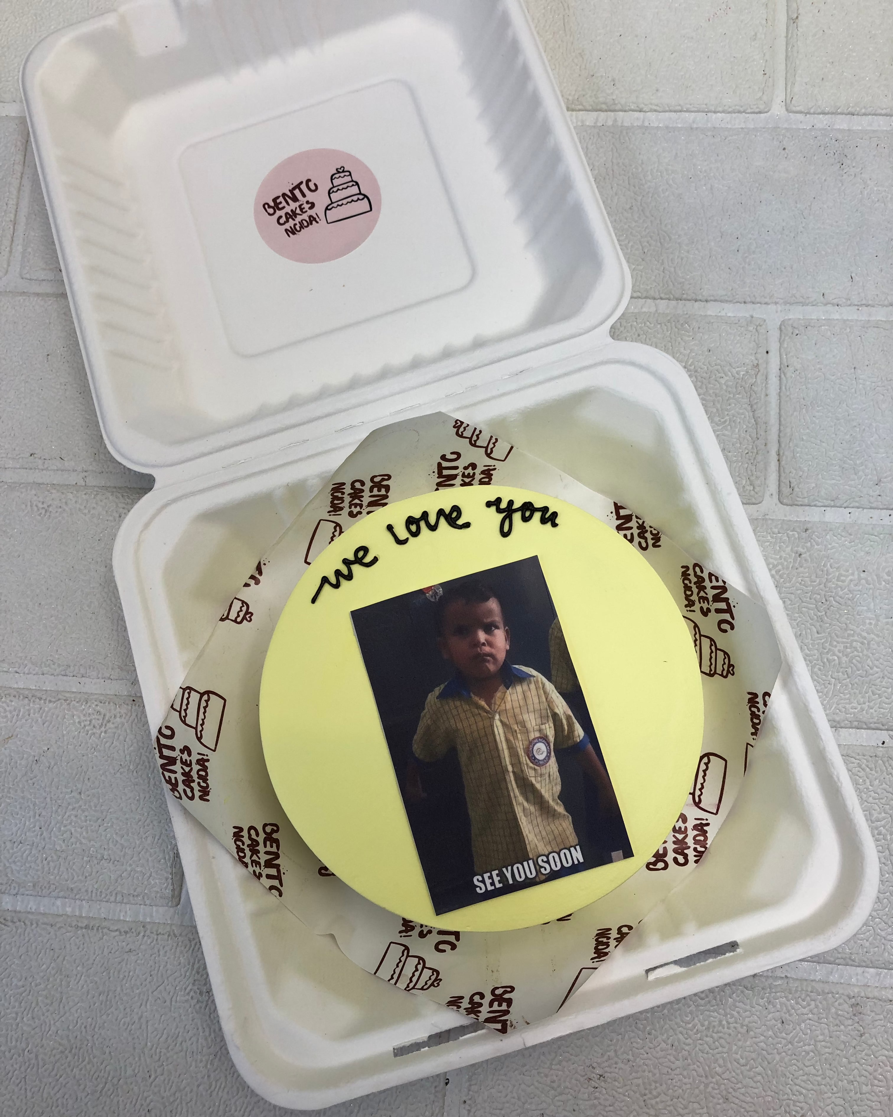 A light yellow bento cake having a school kid friends picrure for birthday.