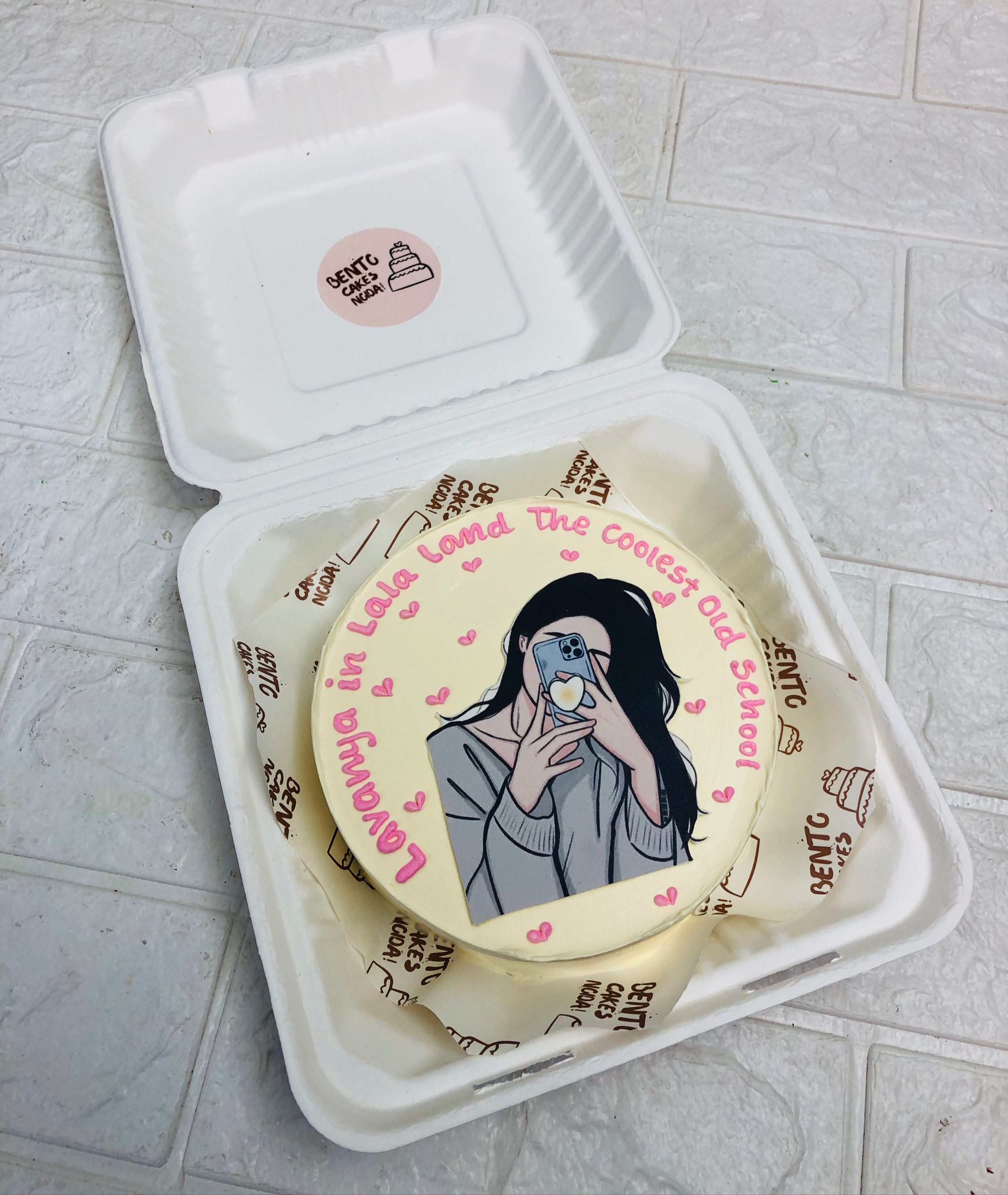 An offwhite bento cake with a girl print taking her selfie.