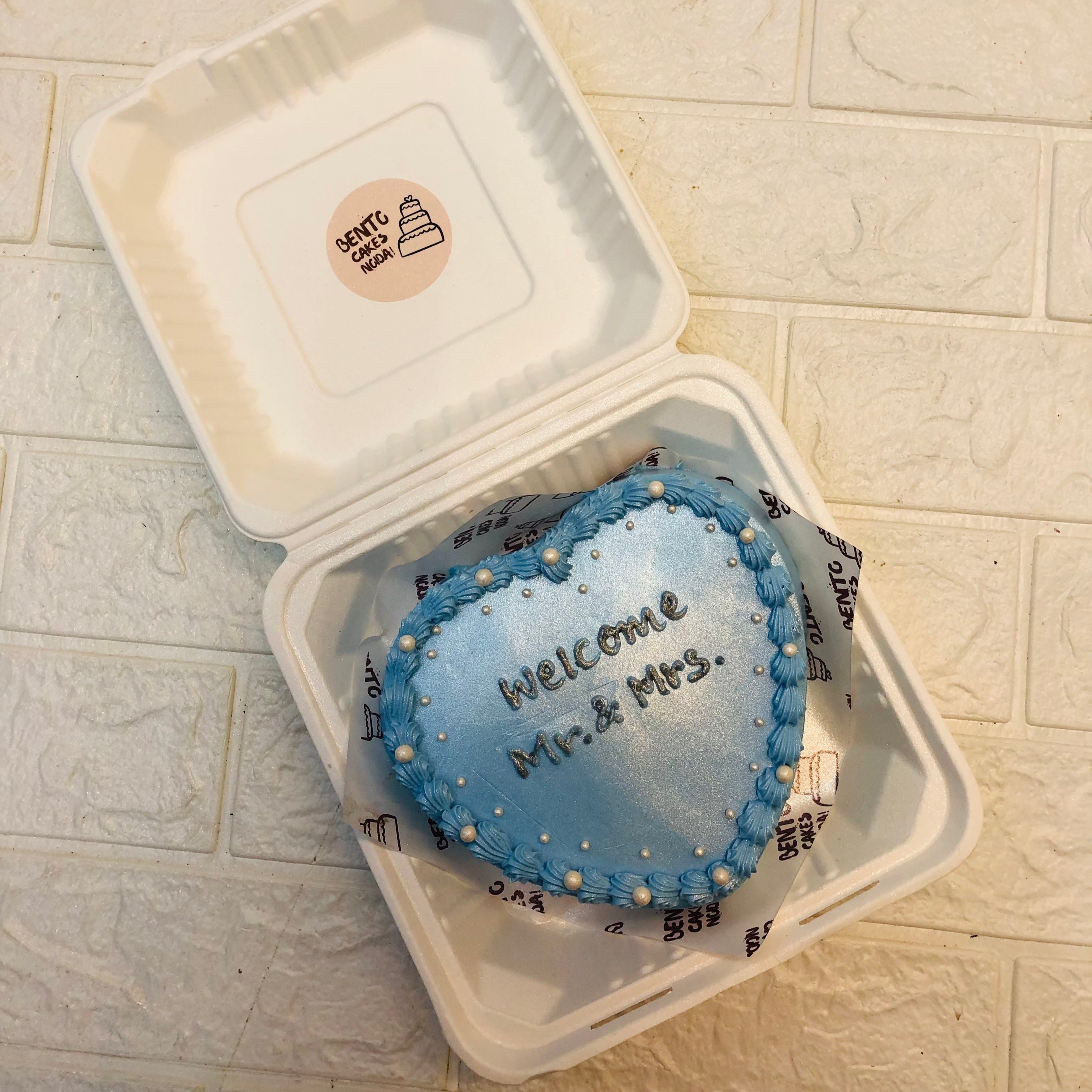 A shiny light blue heart shape cake with golden text on it.