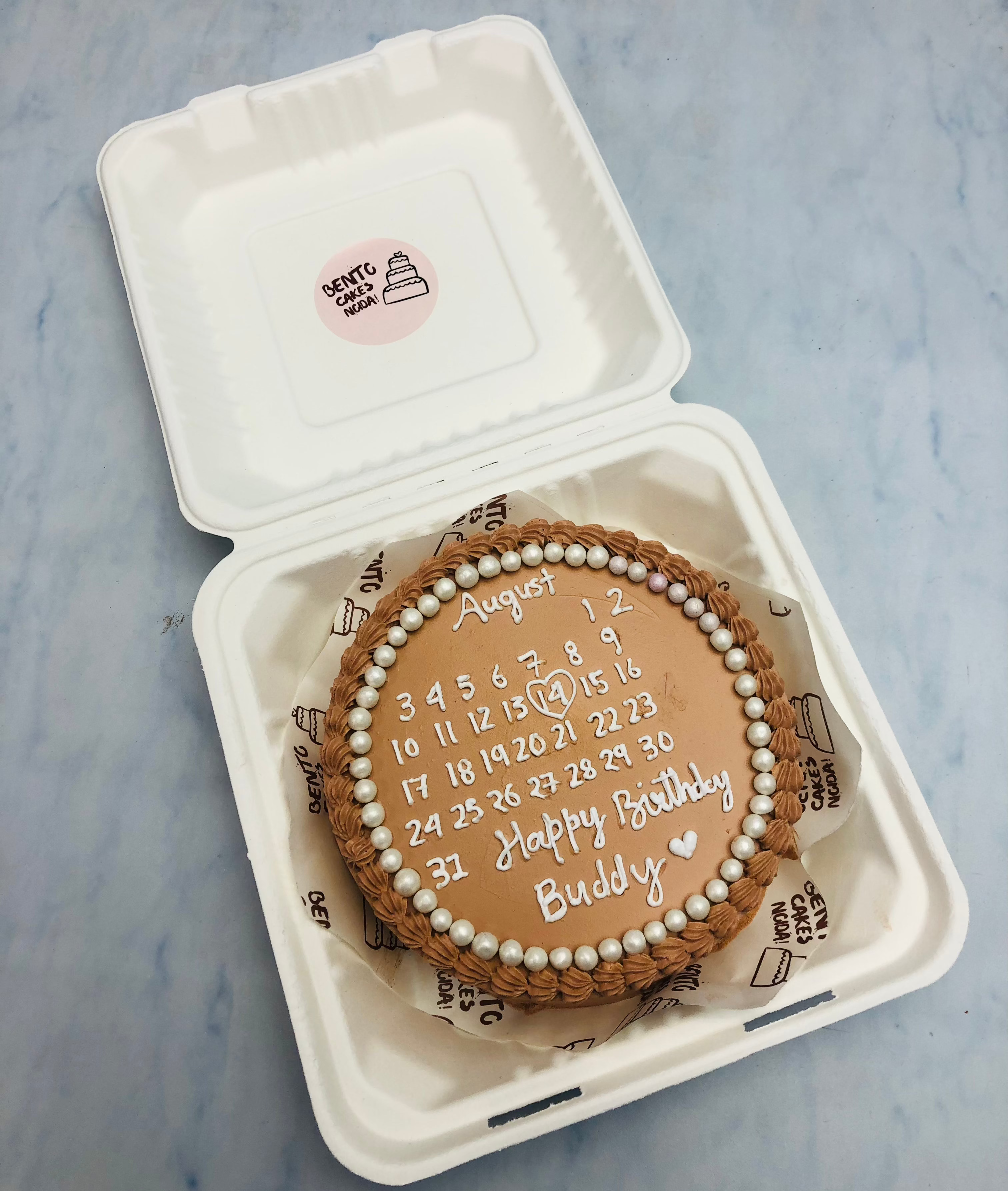 A shiny brown bento cake having white calendar design on it.