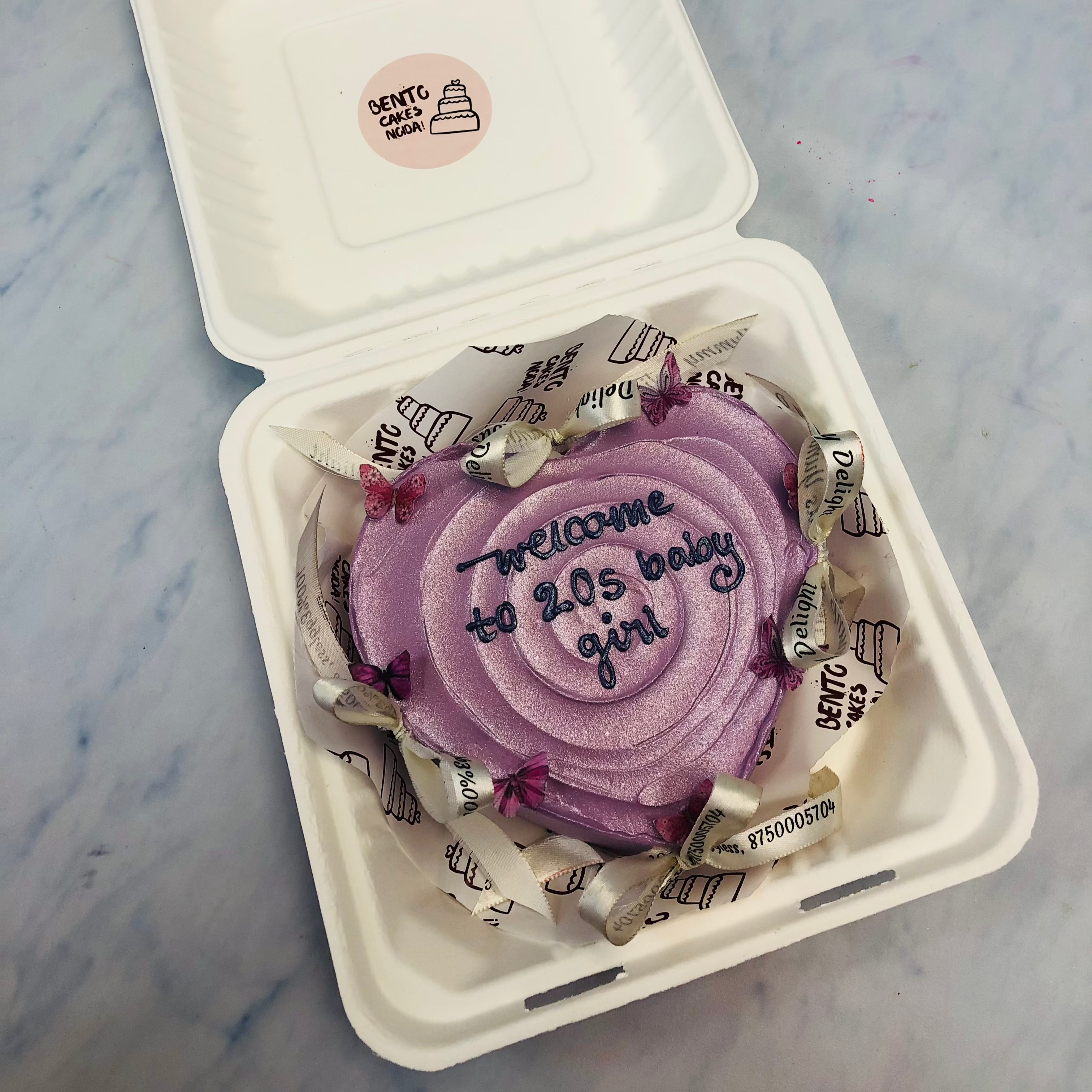 A shiney purple heart shape cake with pink butterlies and white bows on it.