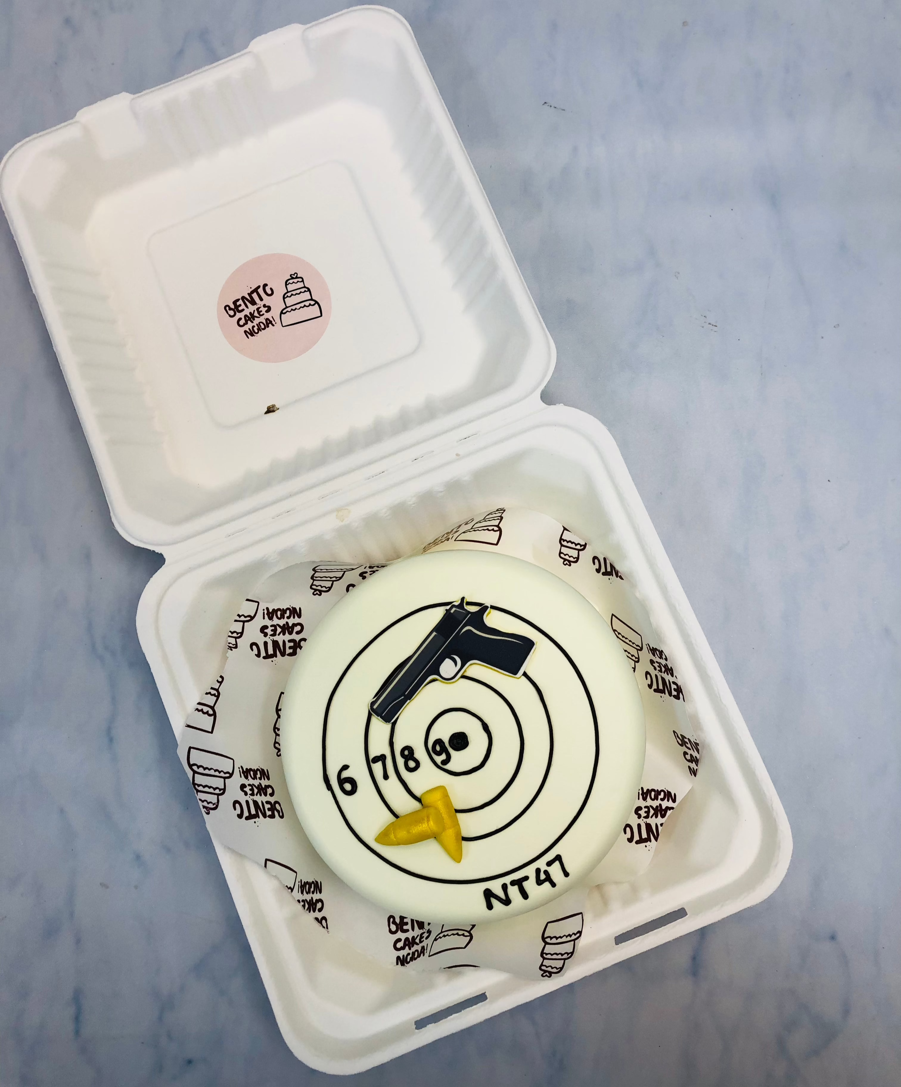 A white bento cake designed on target shooting theme with gun and bullets.