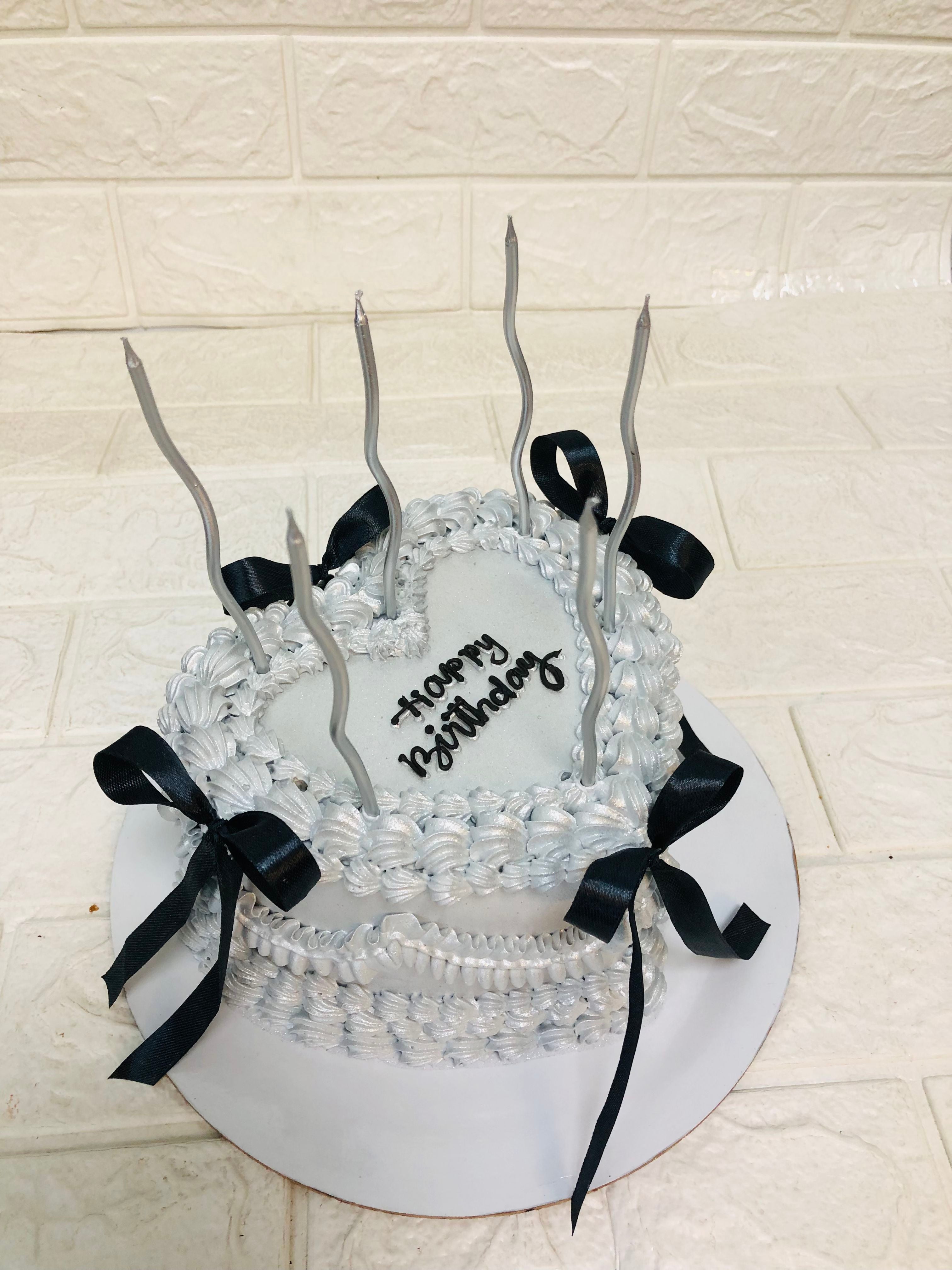 A festive silver heart shape cake featuring candles and a joyful "Happy Birthday" inscription, perfect for celebrating a special occasion.