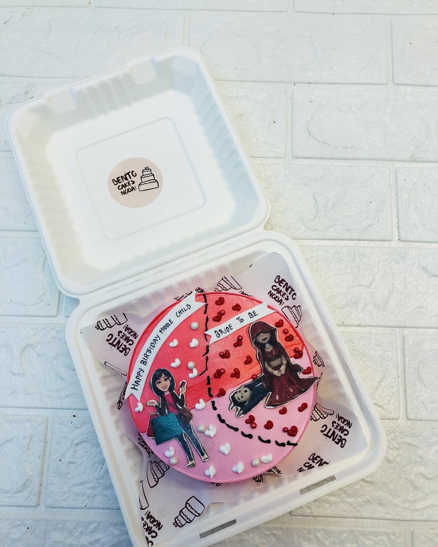 A custom birthday cake from Gentle Cakes, featuring a pink and red design with heart decorations and illustrations of two characters.