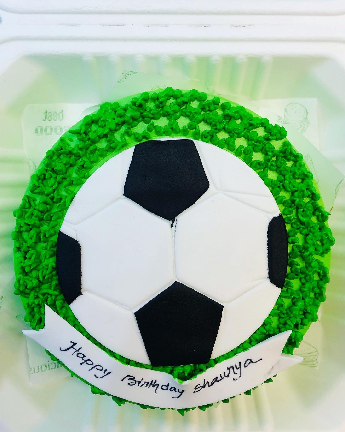 A soccer ball cake displayed in a Styrofoam container, showcasing its intricate design and festive presentation.