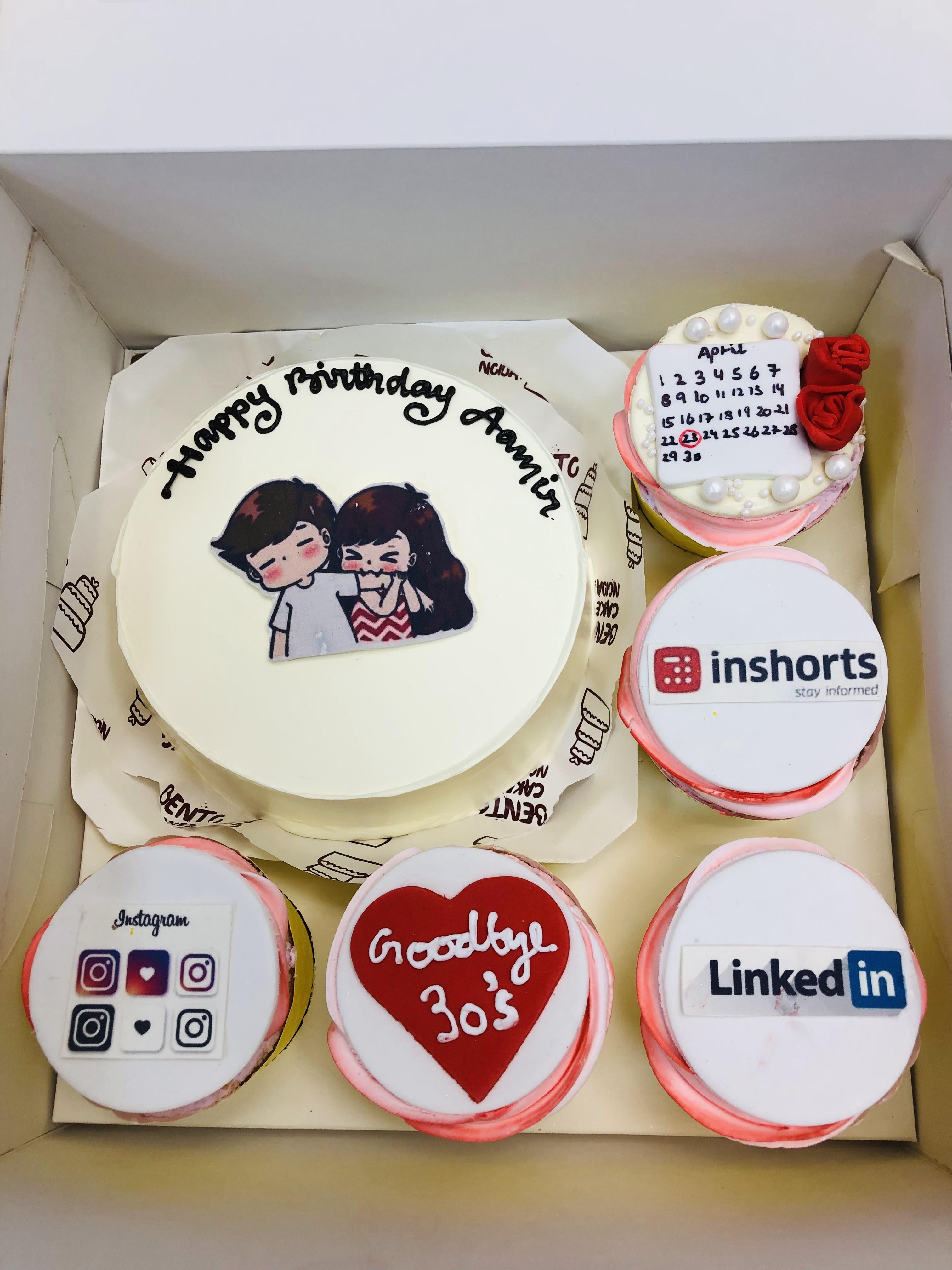 A birthday cake set including a main cake decorated with a cartoon couple and the words "Happy Birthday Aamir," surrounded by five themed cupcakes featuring designs like social media logos and "Goodbye 30's."