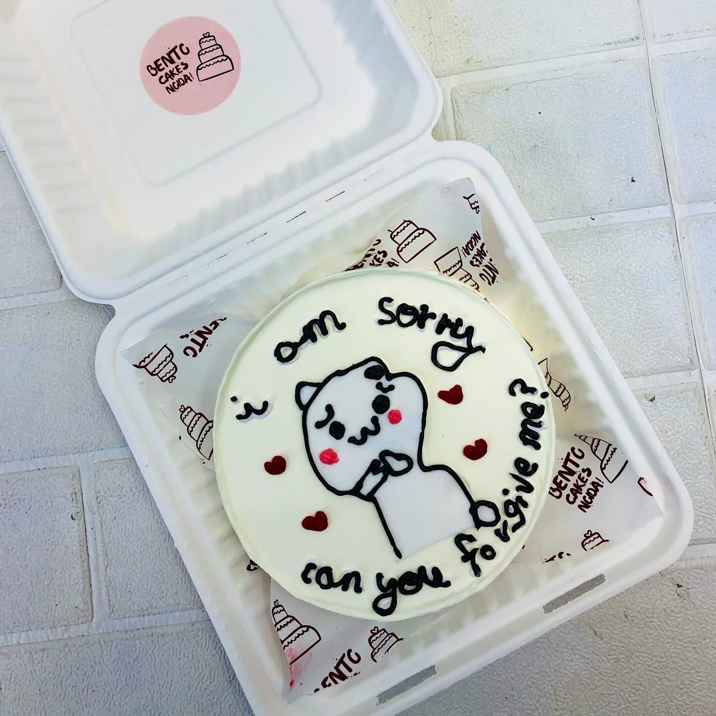 A white cake with cute cartoon drawing and saying sorry.