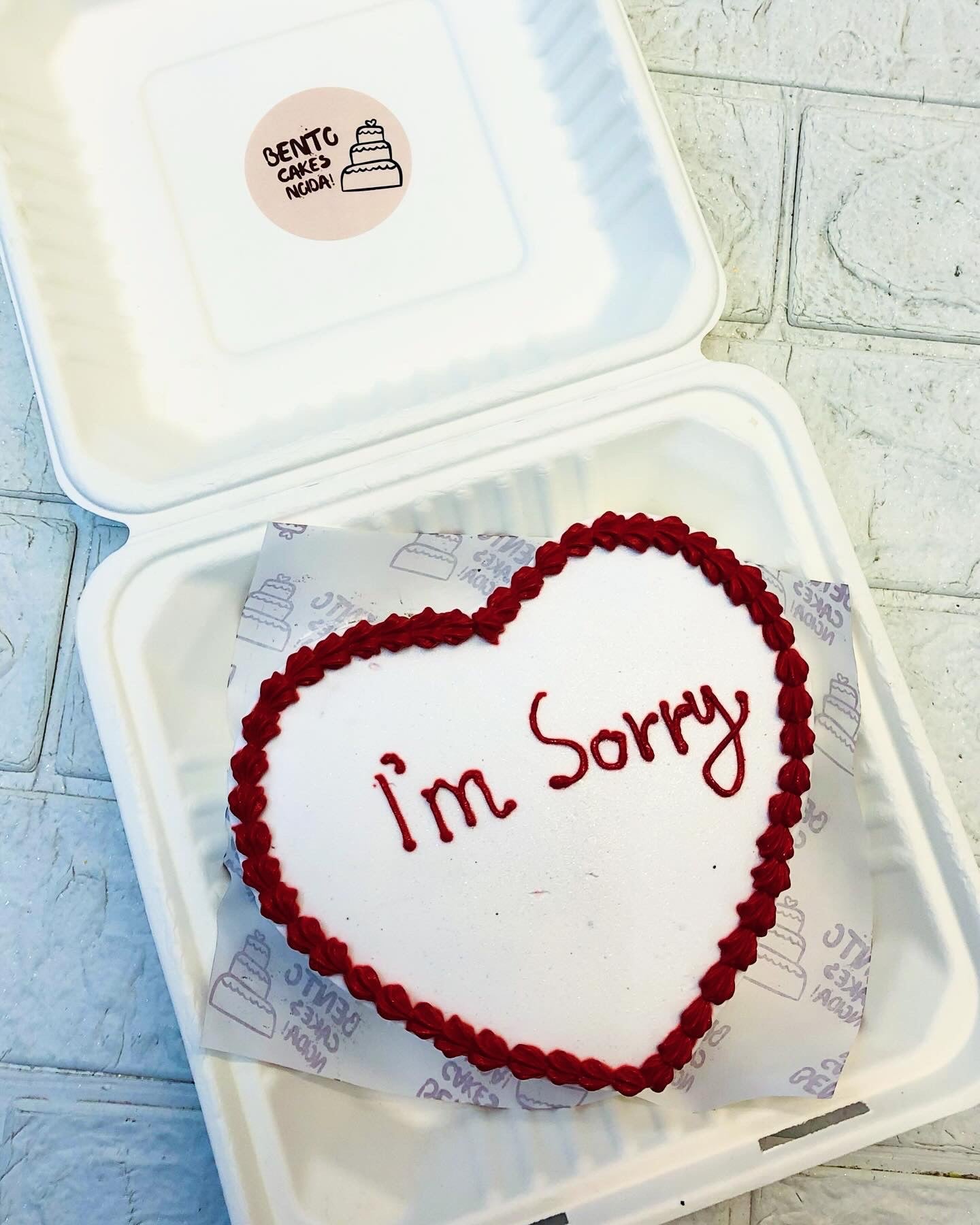 A white heart shape cake covered with red boundary and a "I'm Sorry" text written on it.