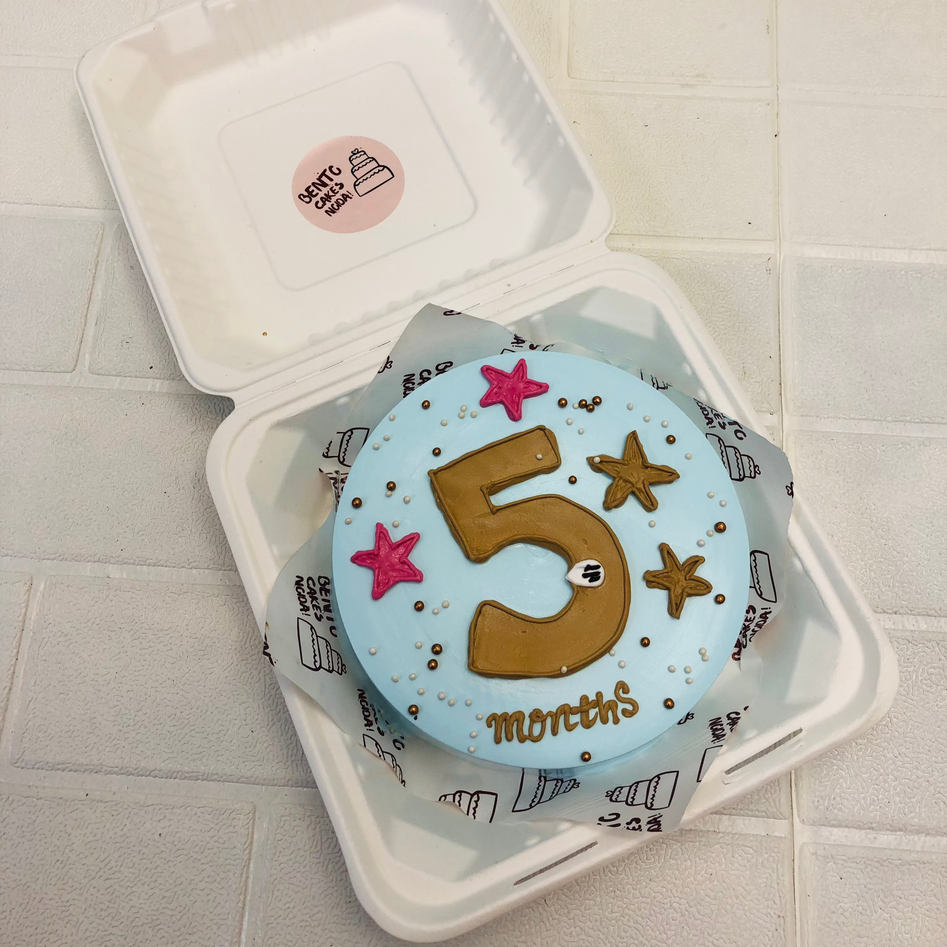 A sky blue bento cake decorated with 5 number design and pink, brown stars.