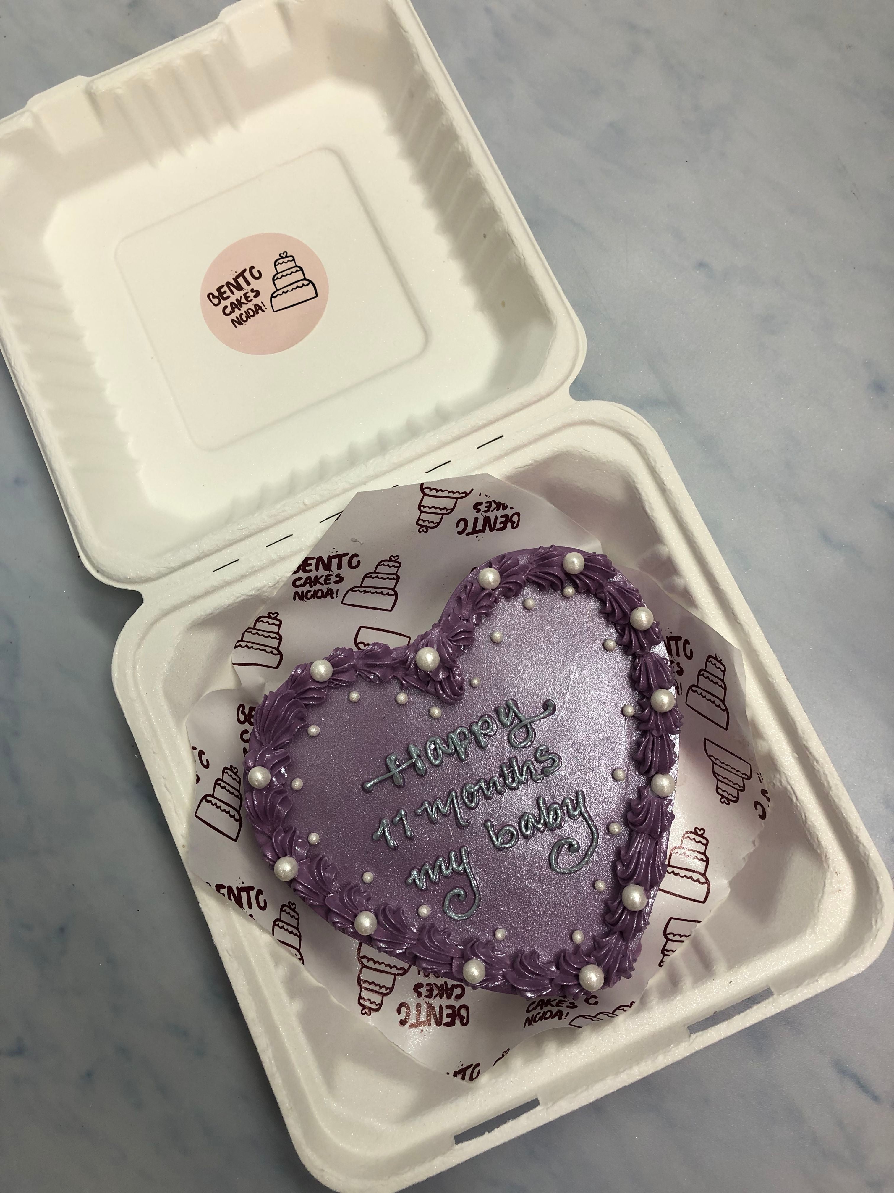 A shiney purple haert shape cake with white spinkles and text wruitten with grey icing on it.