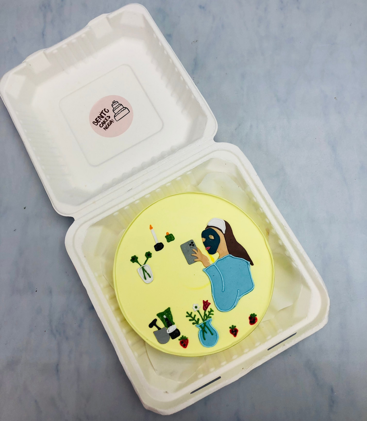 Round cake featuring a hand-drawn illustration of a person reading a book, surrounded by plants and candles.