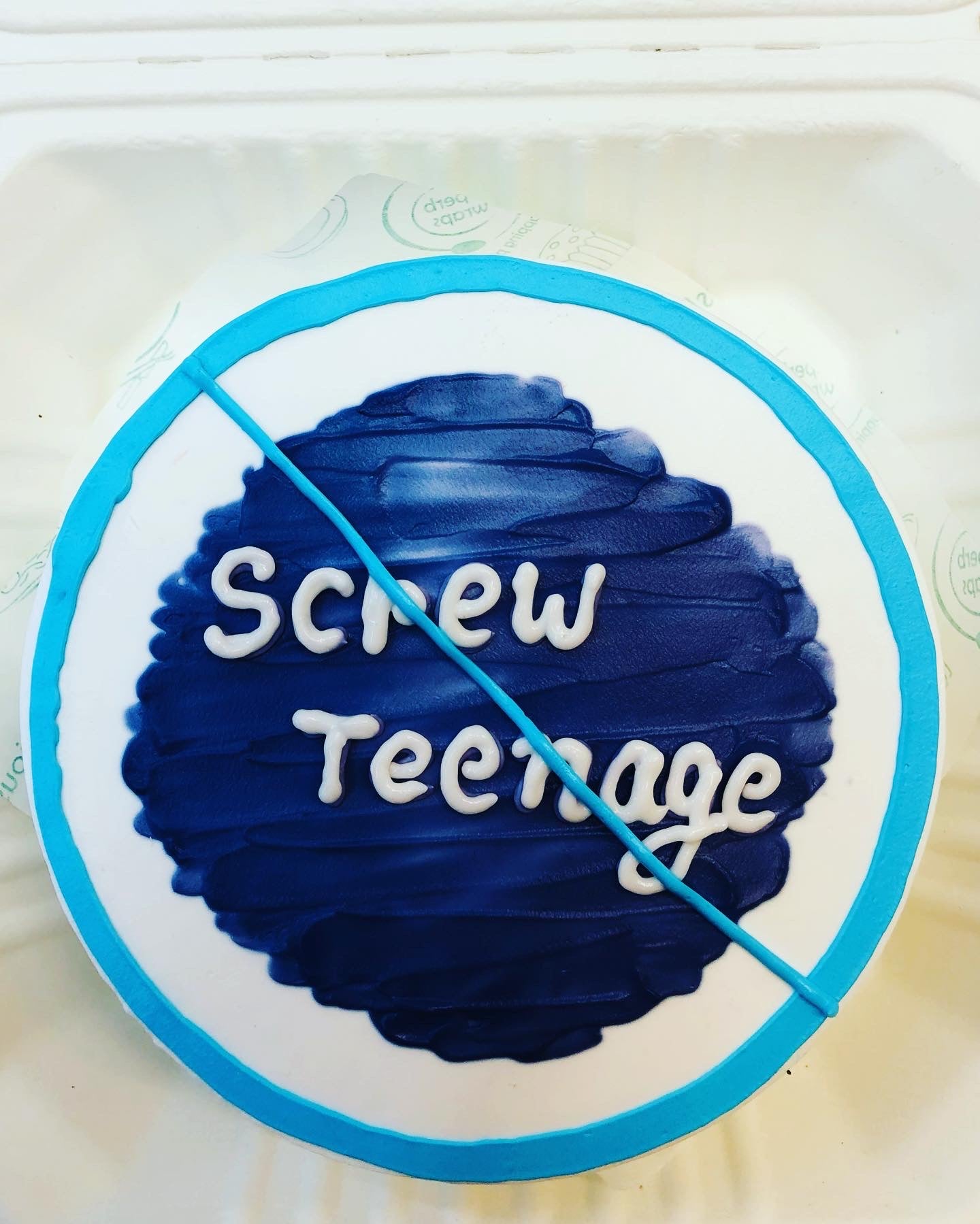 A white cake decorated with blueicing on its center and a text "Screw Teenage" written on it and a circle designed on its surrounding with sky blue color.
