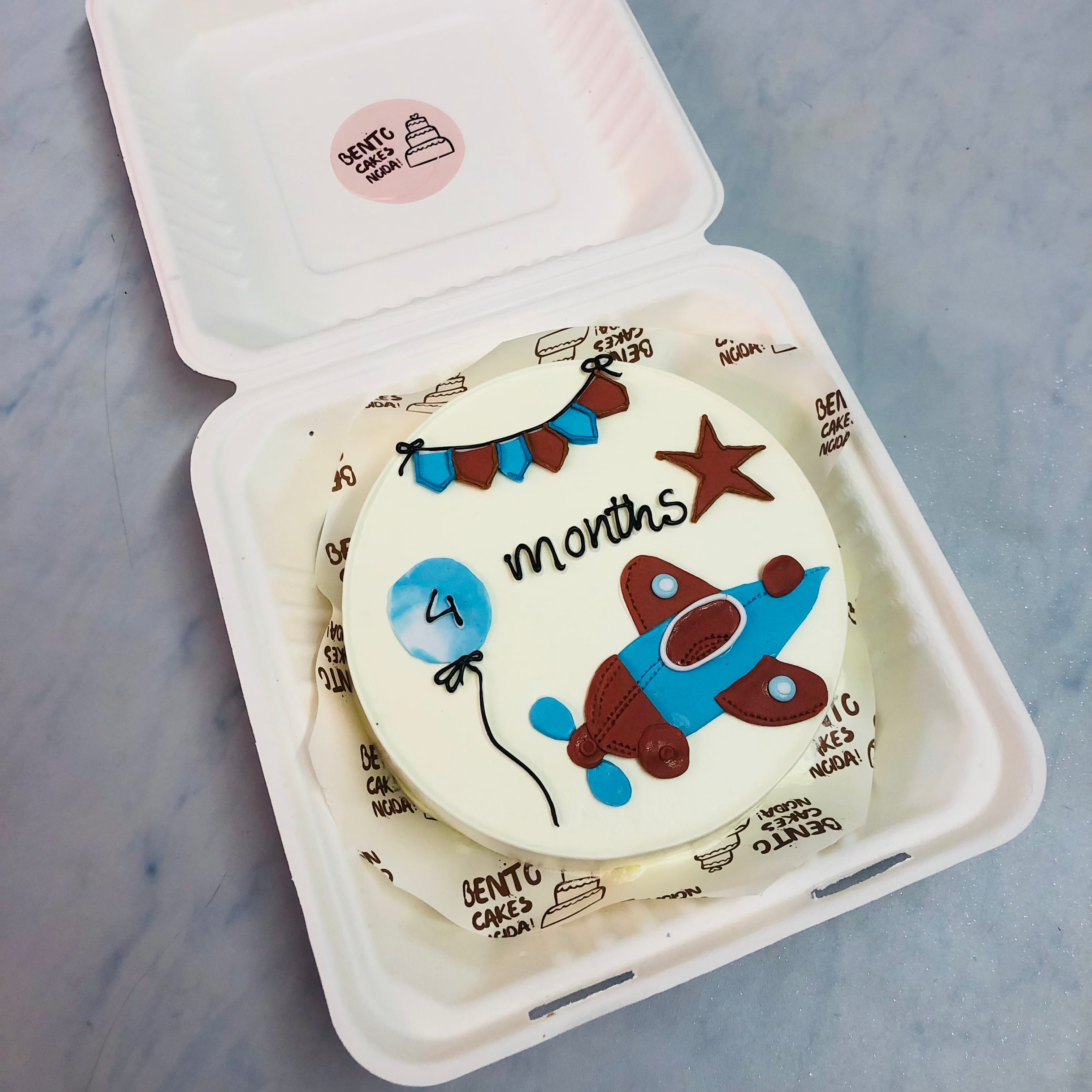 An ofwhite cake withn blue and brown plane design with star and balloon.