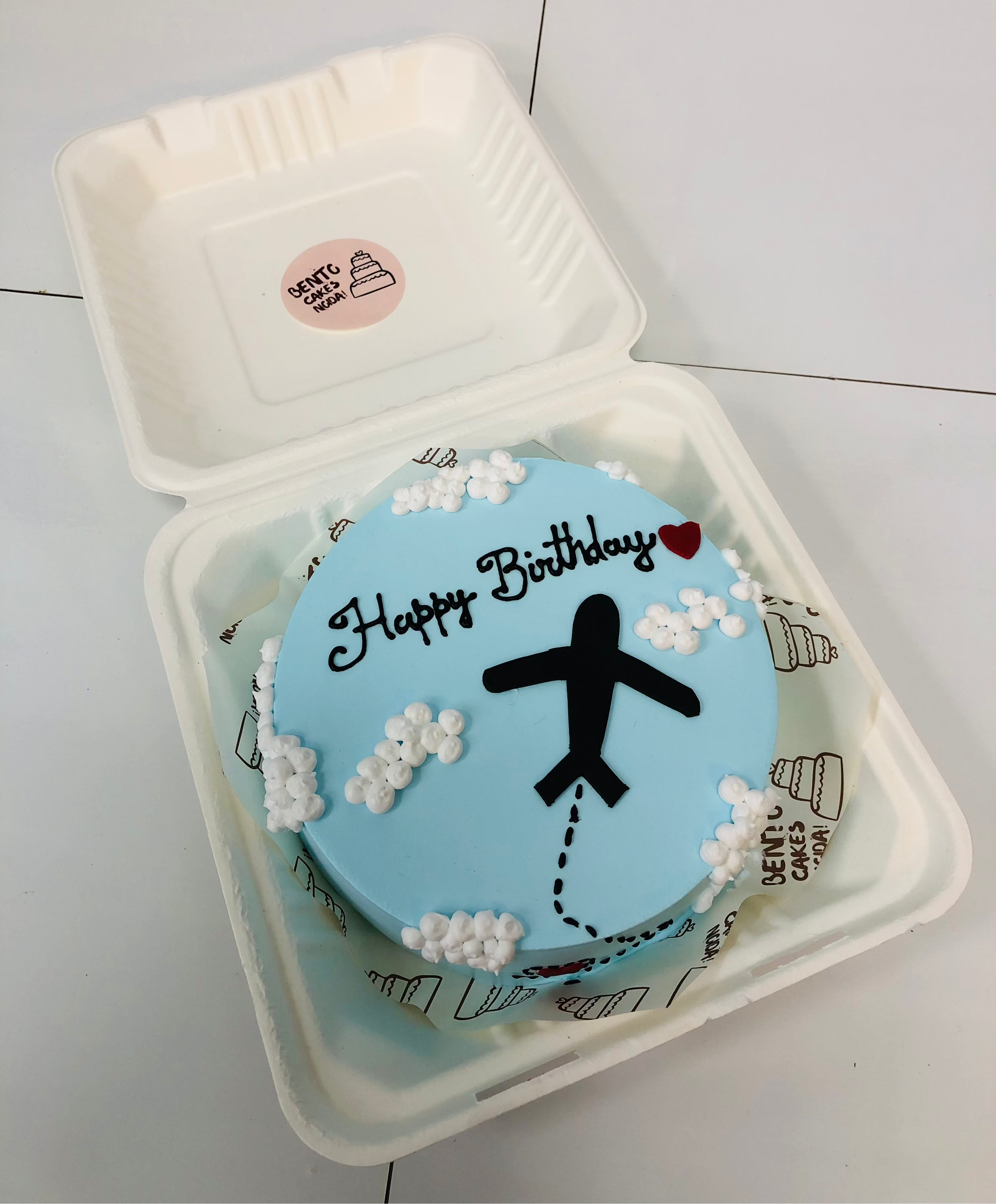 A light blue bento cake having clouds and a flying aeroplane.
