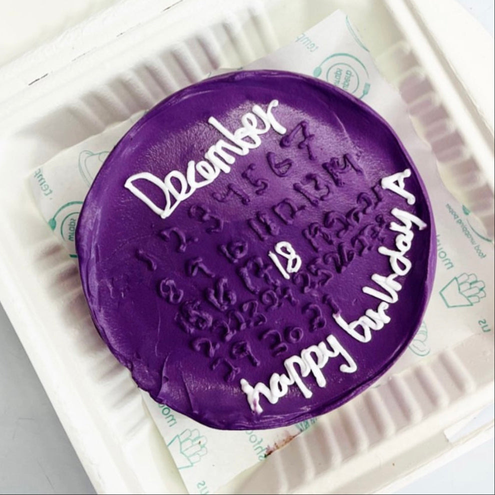 A vibrant purple cake in a soft foam container, adorned with a written message on its surface.