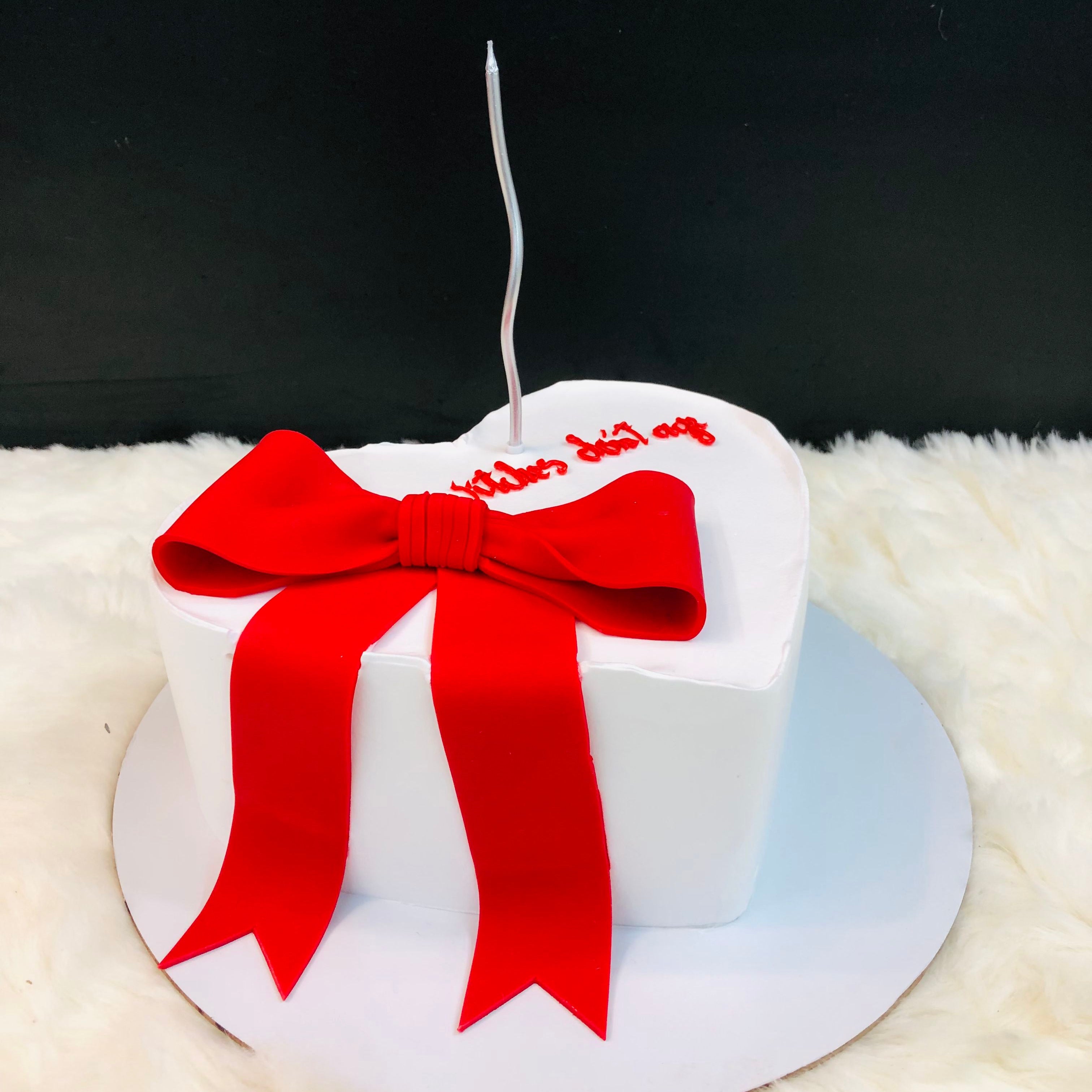 A white cake adorned with a vibrant red bow on top, elegantly presented for a special occasion.