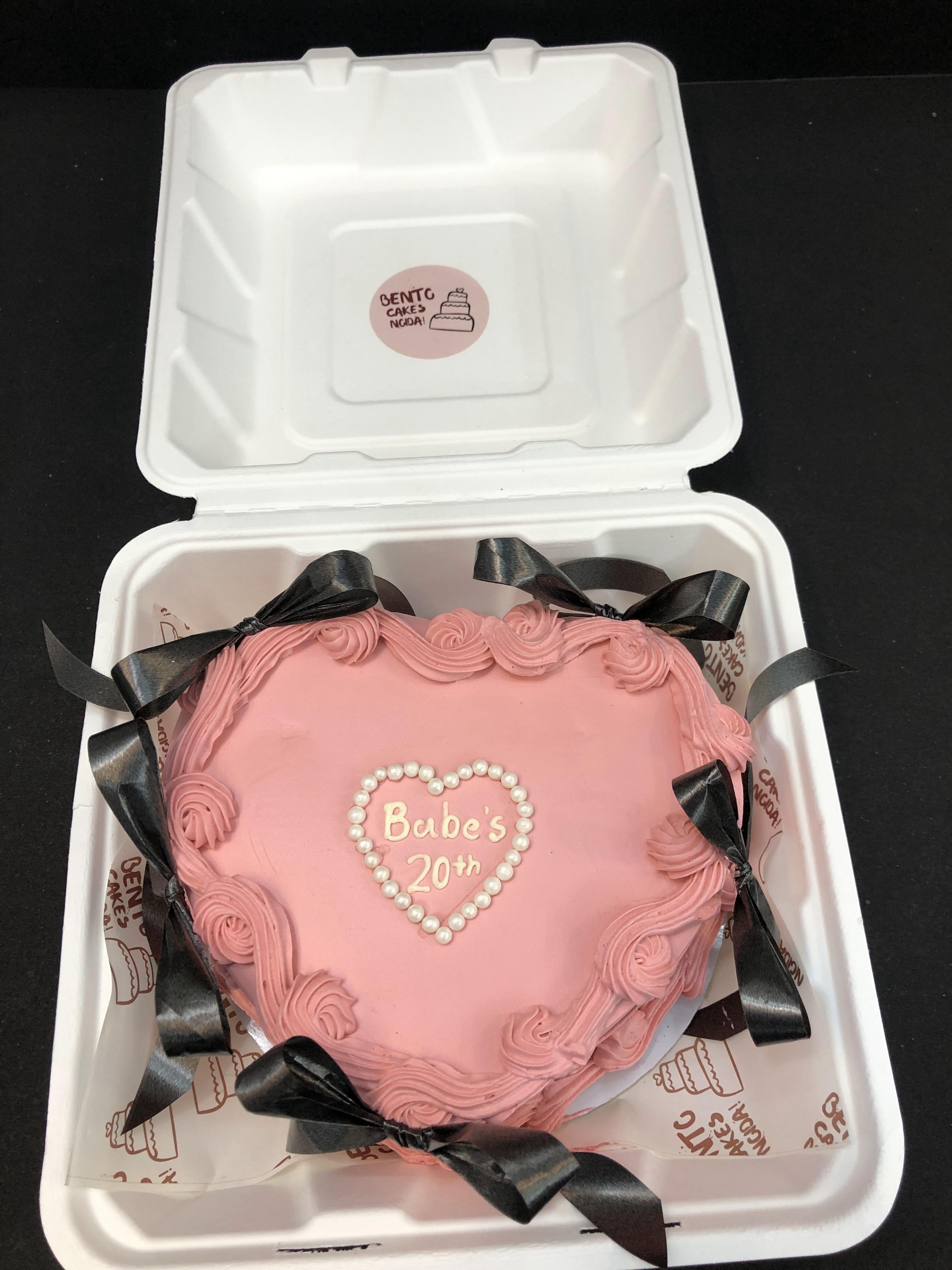 A pink heart shape bento cake with black bows on it.