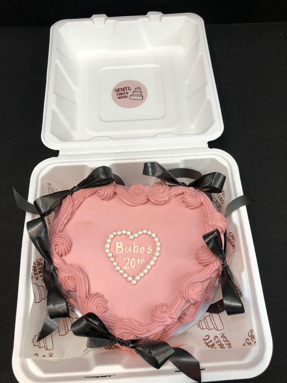A pink heart shape bento cake with black bows on it.