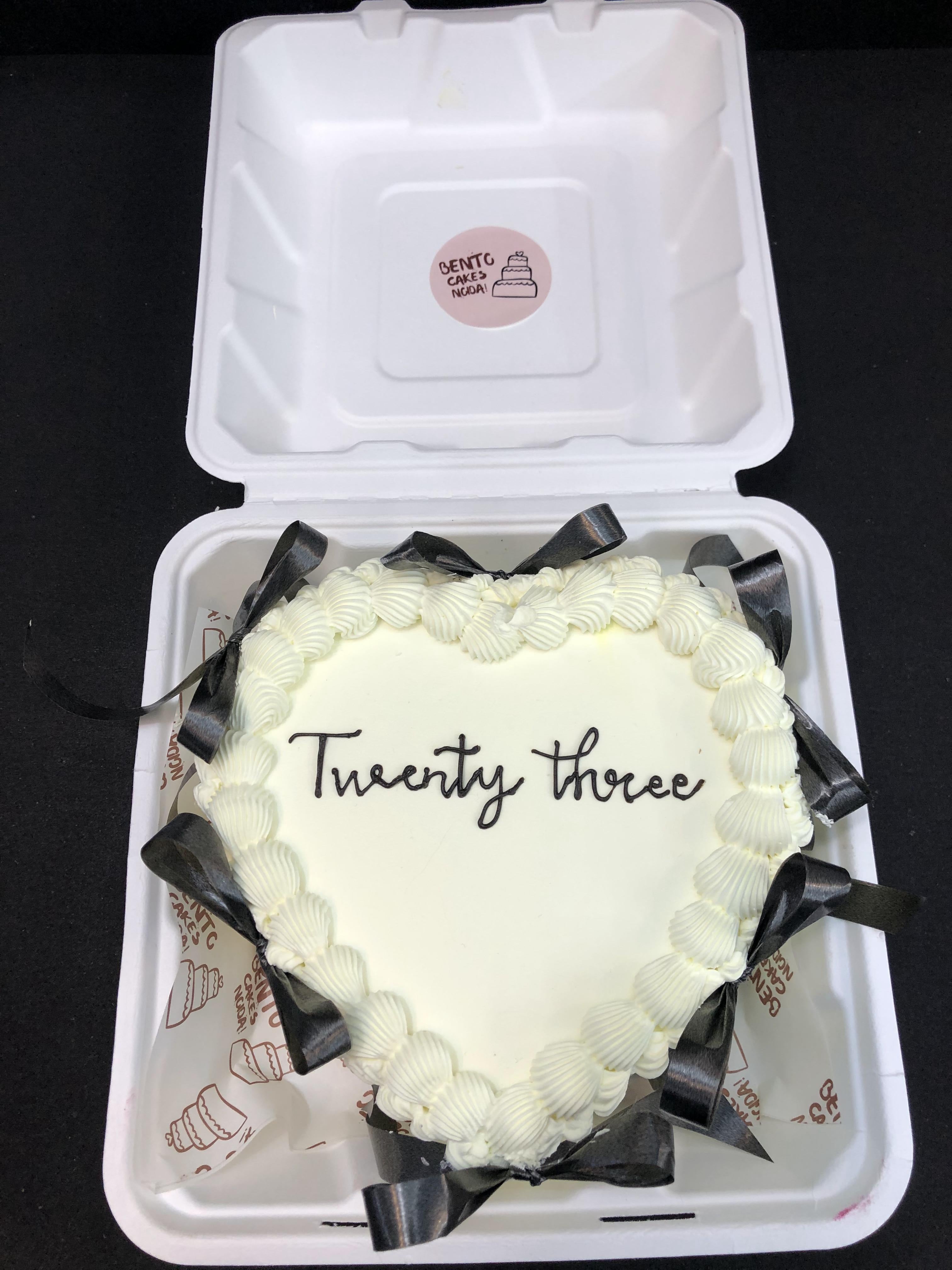 A white heart shape cake with black bows and white boundaries.