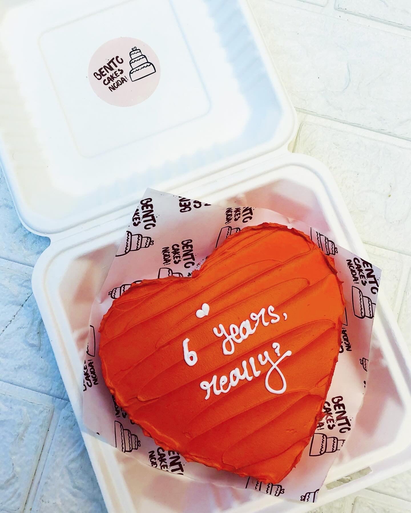 A dark red icing heart shape cake with wavy design on it's top and a loving text written with white icing on it.