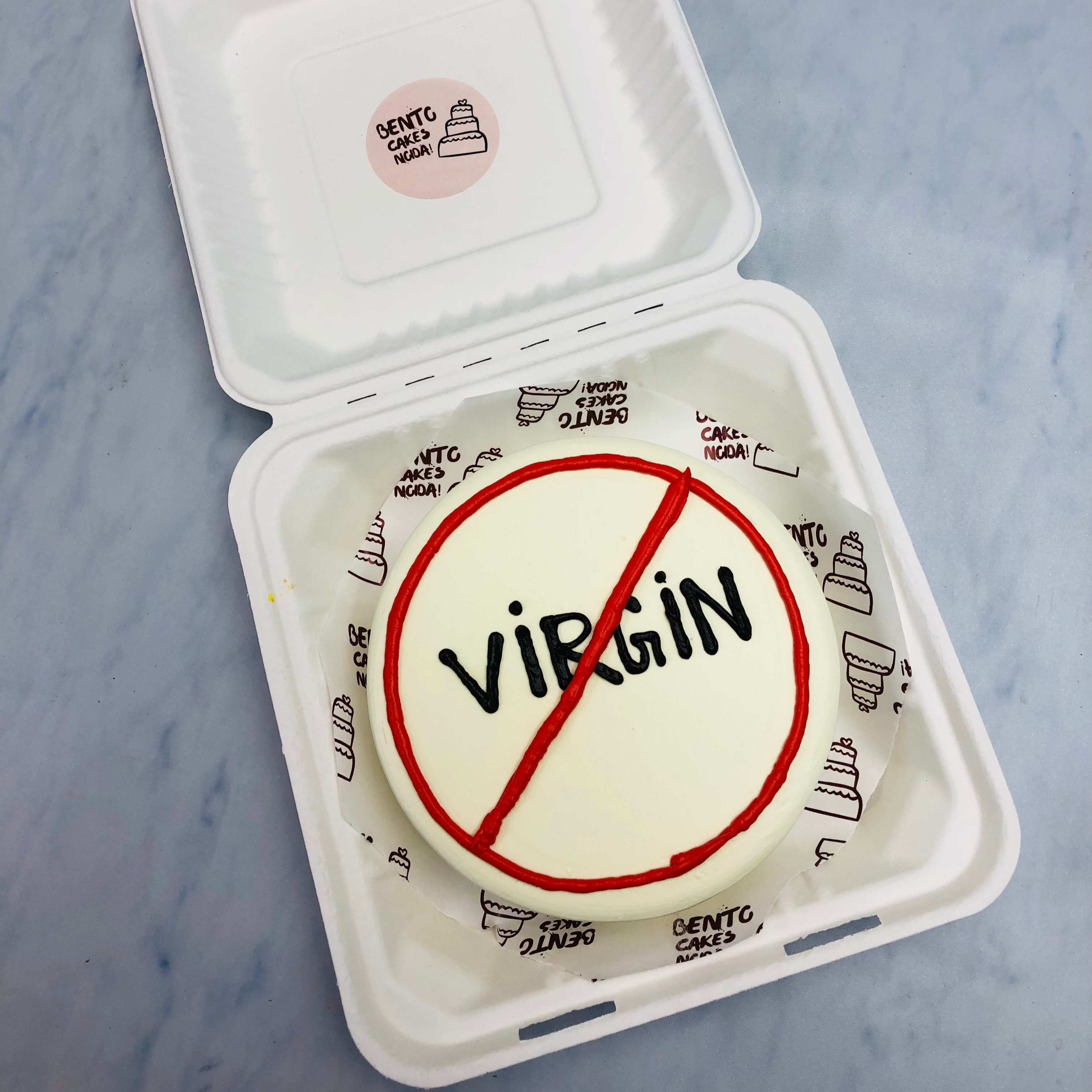 A white bento cake with a "ViRGiN" text written with blacvk color and cuted with red color.