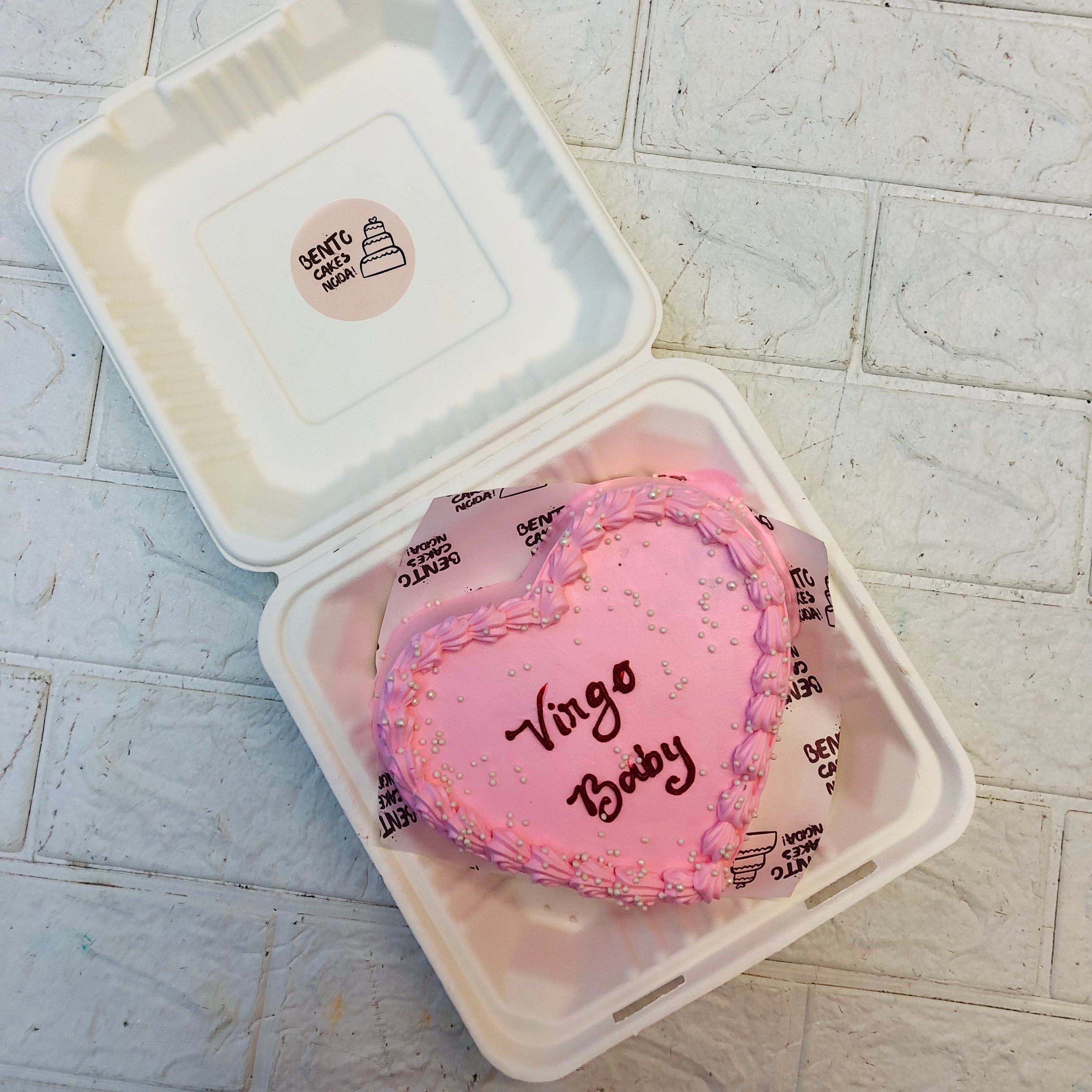 A baby pink heart shape cake decorated with silver sprinkles and a text written with red color.