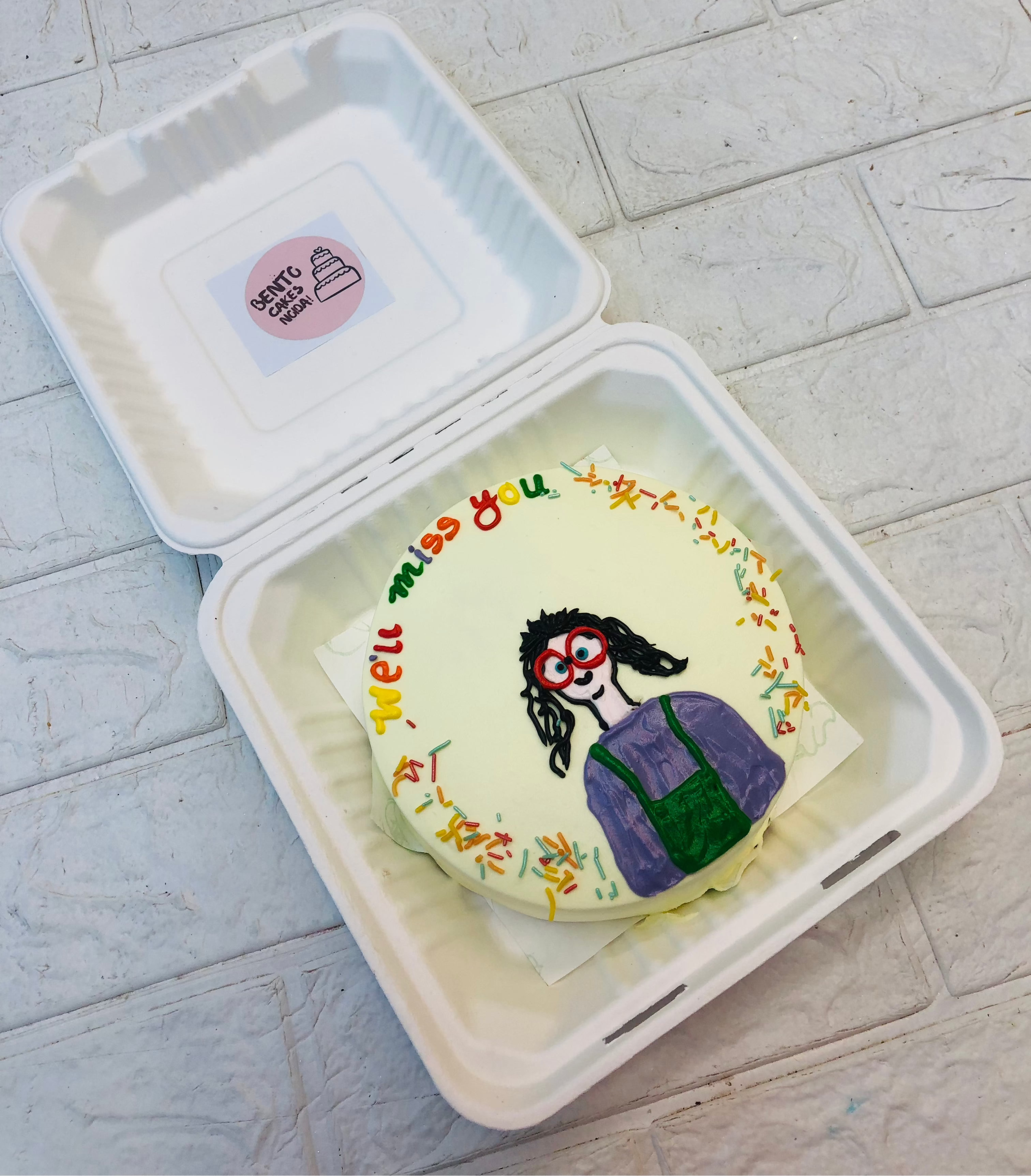 A cartoon girl designed on an offwhite bento cake with a colorfl text "We'll miss you"
