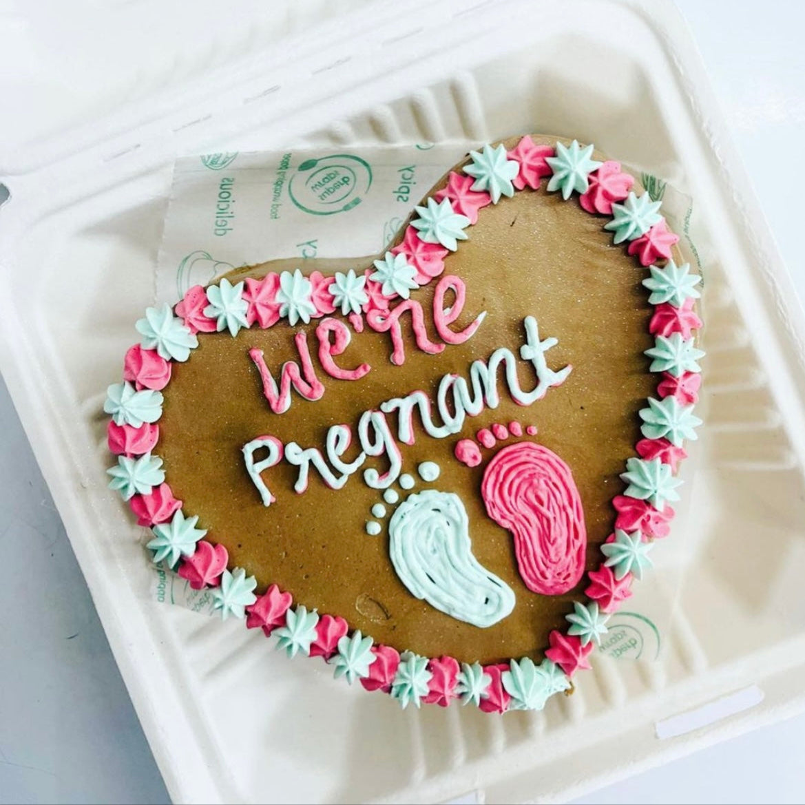 A charming cake adorned with pink and green icing, proudly displaying the message "We're Pregnant" in a fun design.