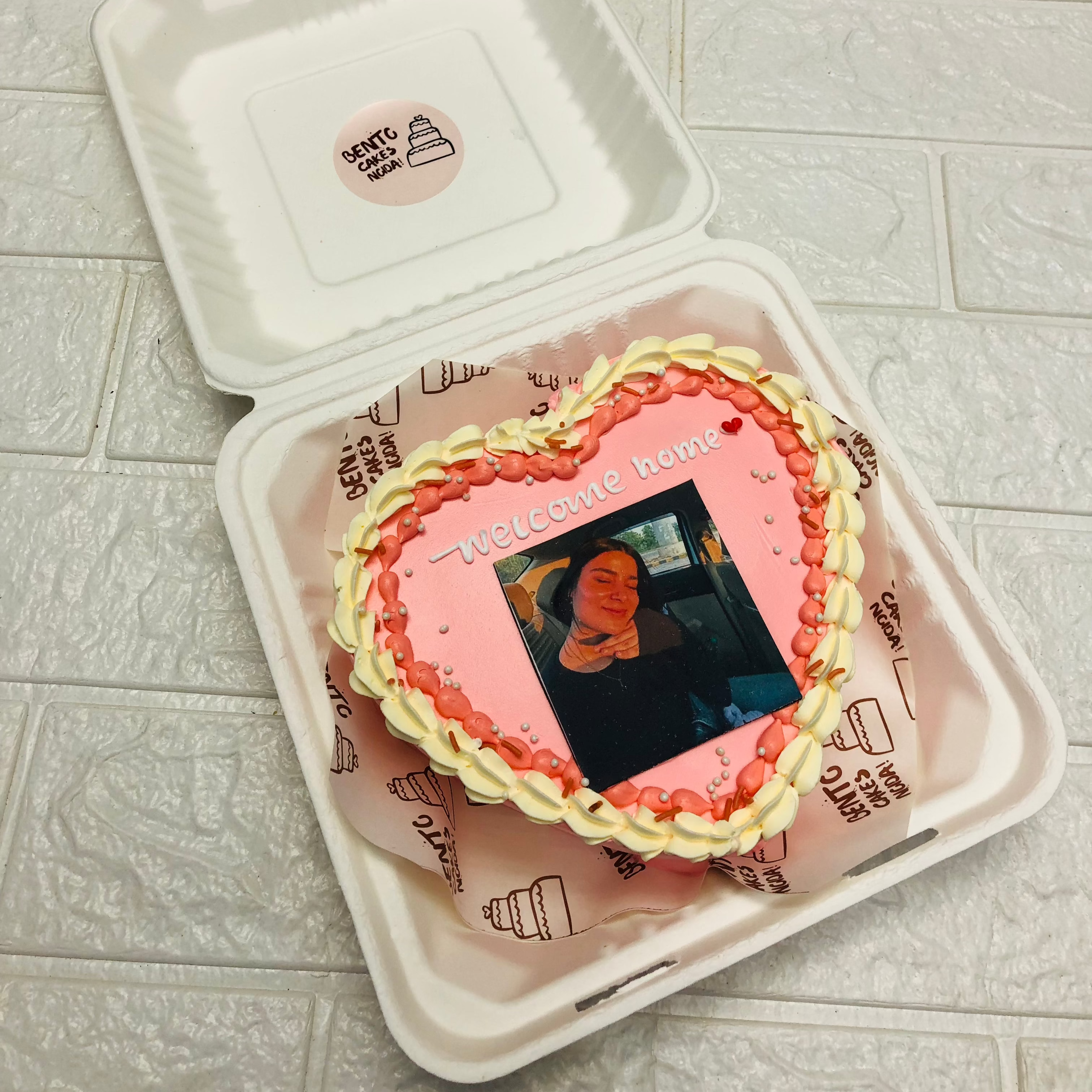 A light pink cake with a photo print and a yellow-red truffle design all arount it's boundary.