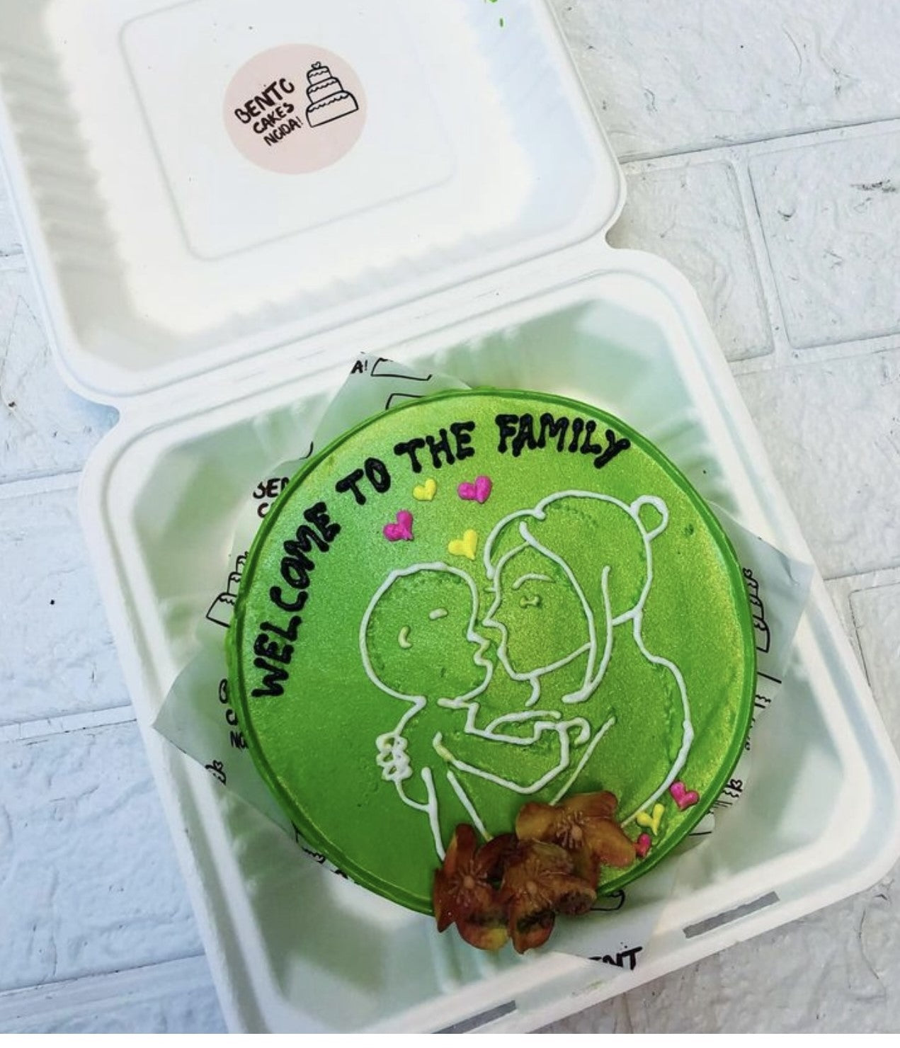 A green color bento cake with a mother and baby sketch on it and decorated with hearts and florals.
