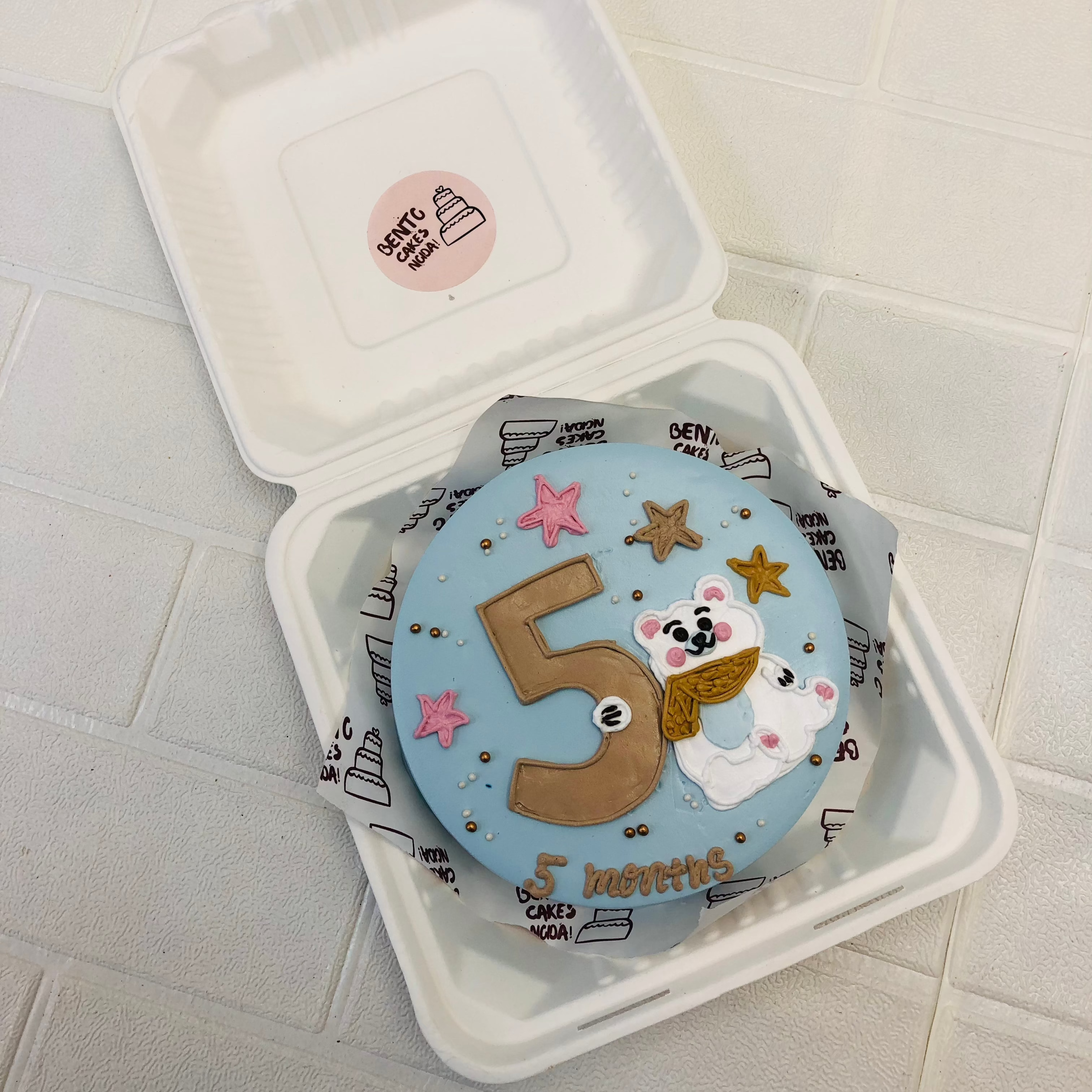 A light blue cake with a white bear design and 5 number drawing with colorful stars.