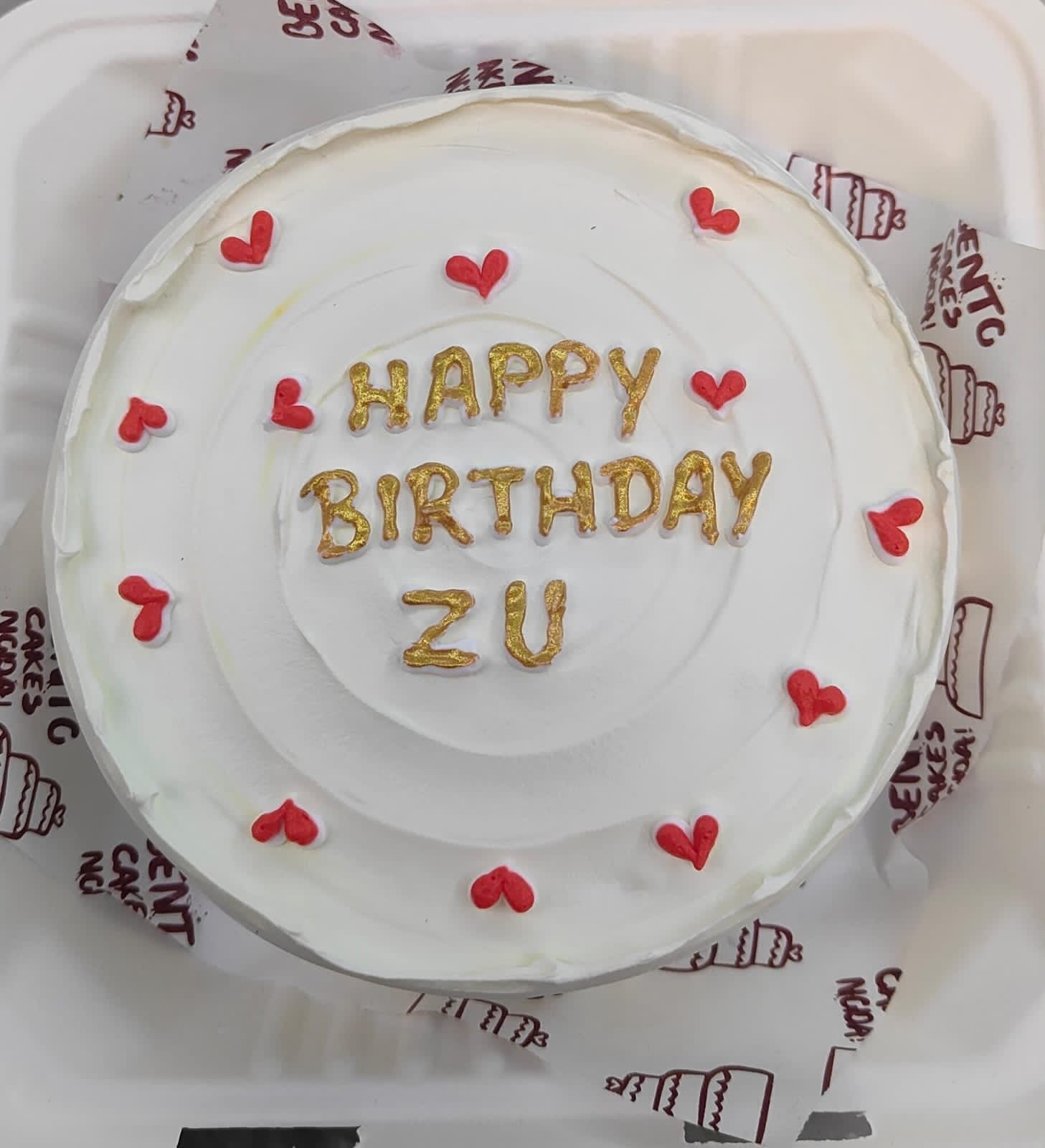 A white bento cake with a golden text "HAPPY BIRTHDAY ZU" and full of red hearts.