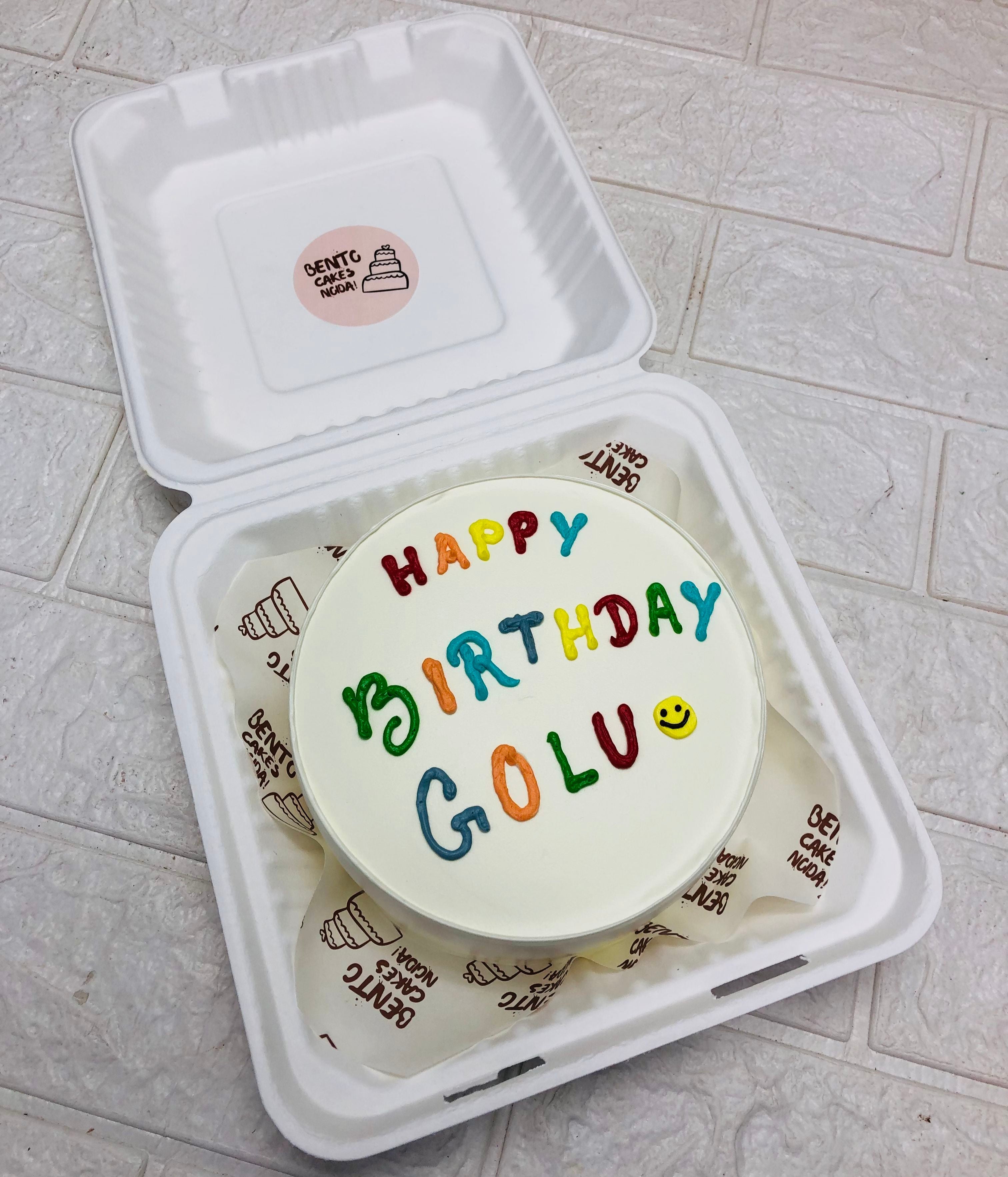A playful white bento cake with colorful text with a smily emoji.