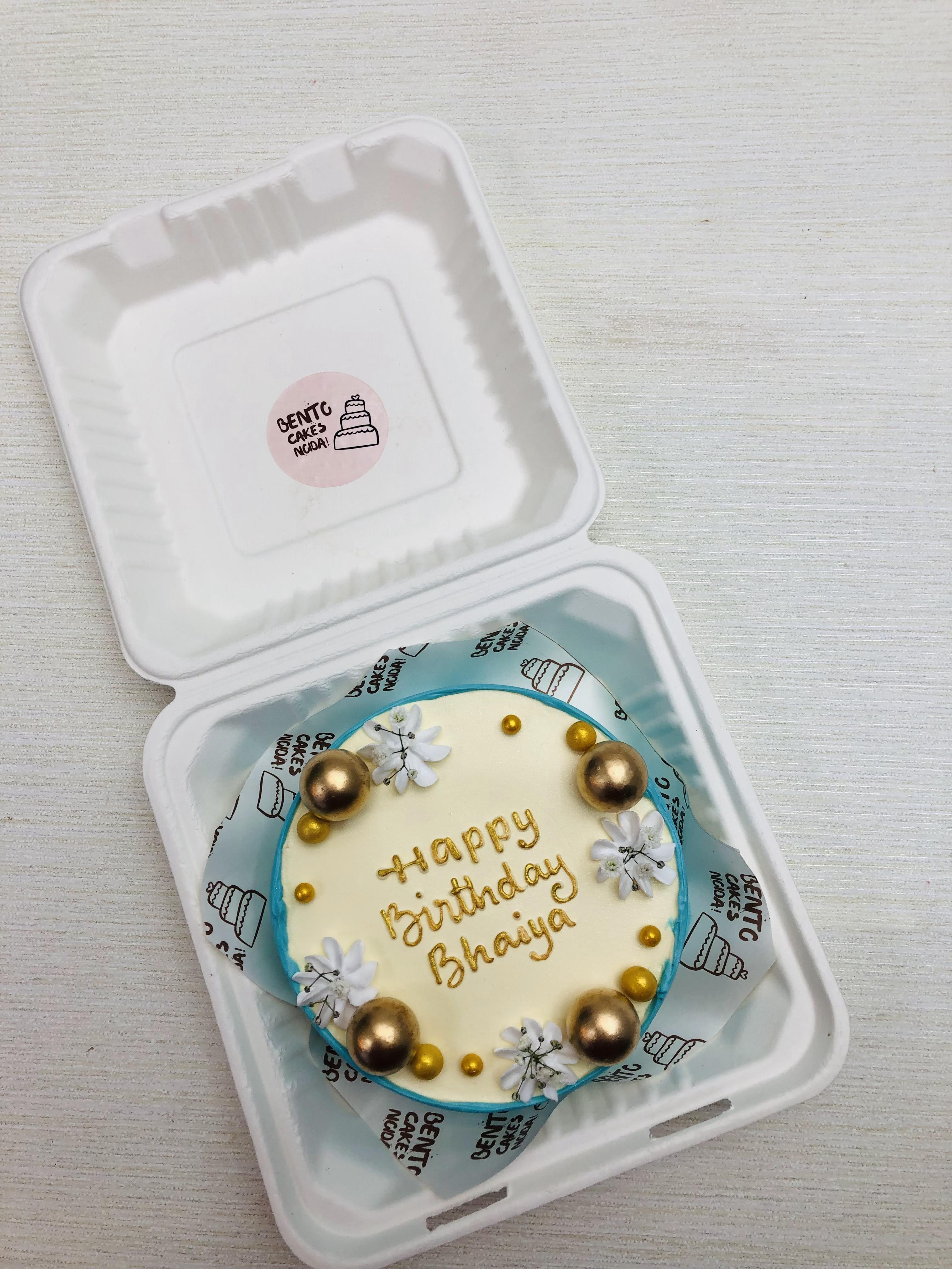 An aesthetic blue and offwhite cake with white florals and decvorated with golden balls on it.