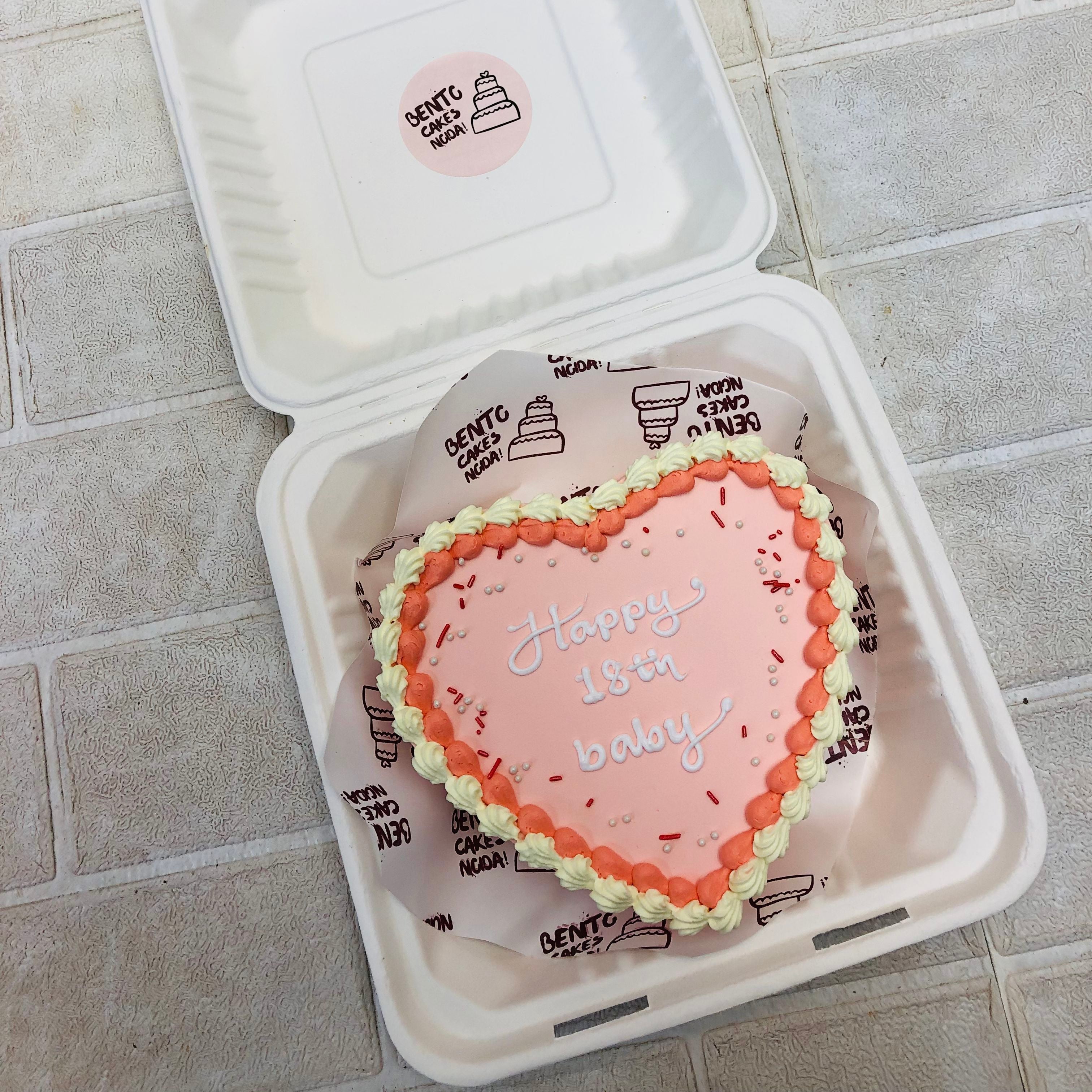 White color heart shape birthday cake in a bento box having offwhite and red boundries.