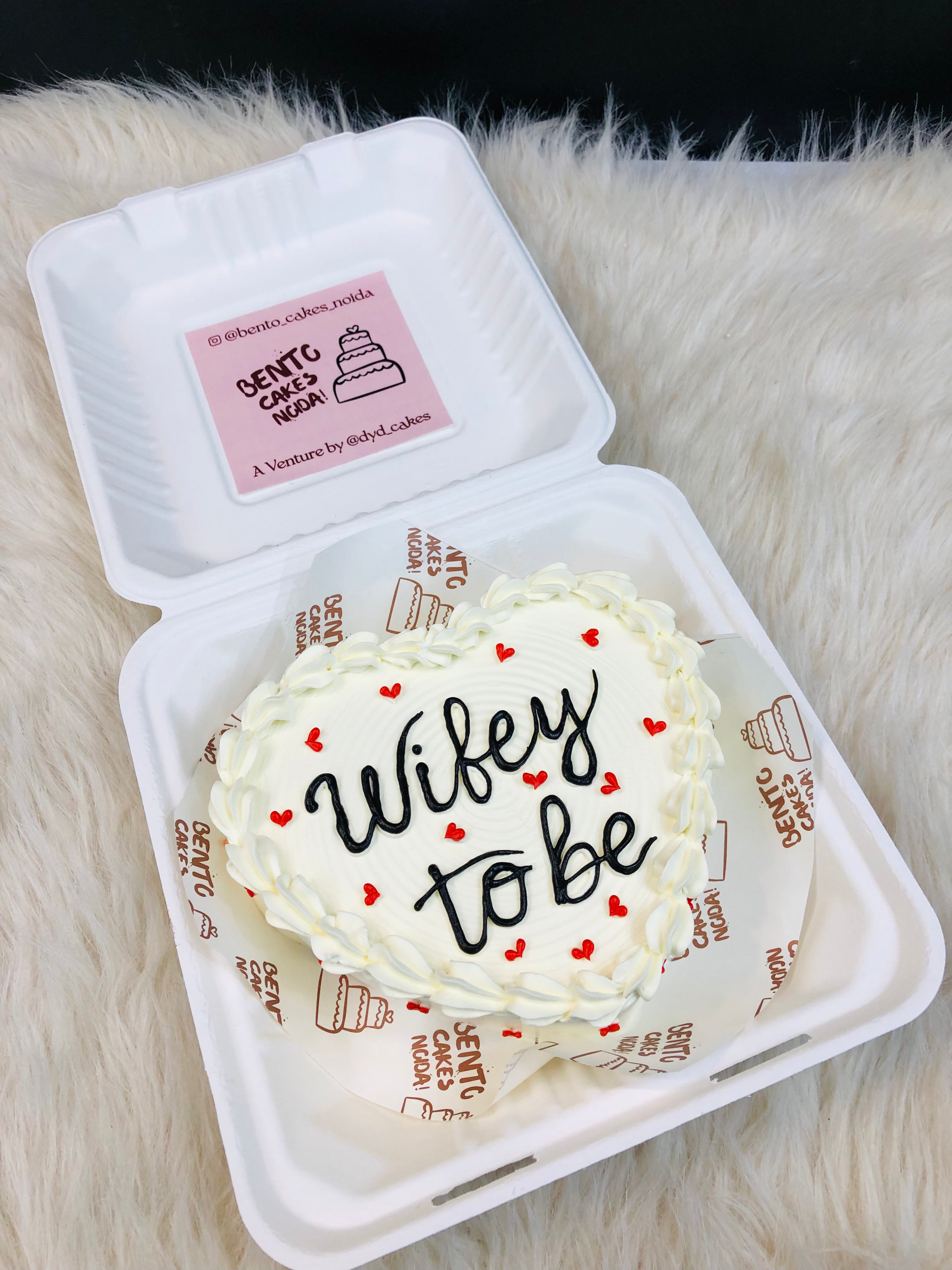 A white heart shape bento cake with white truffle on it's boundary and a "Wifey to be" text written with black icing on it.