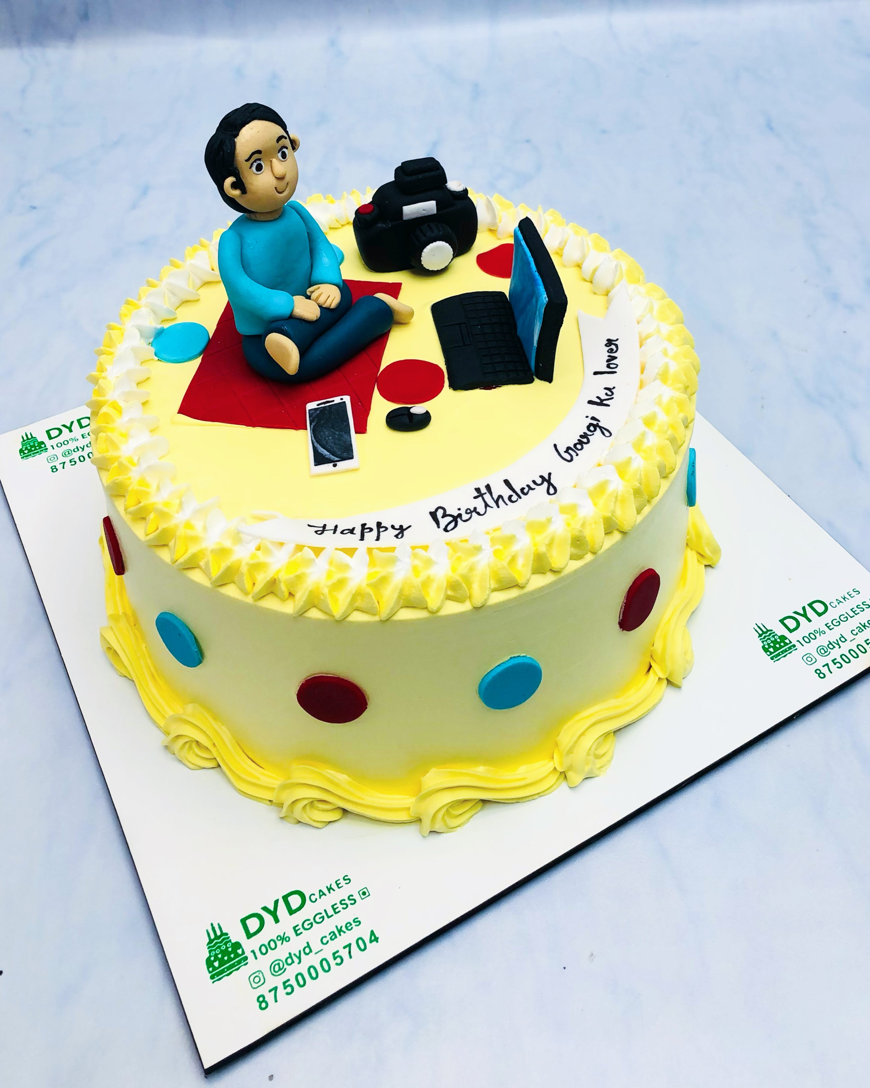 A man sits in a chair with a camera, laptop next to a birthday cake, focused on calculations for the celebration.