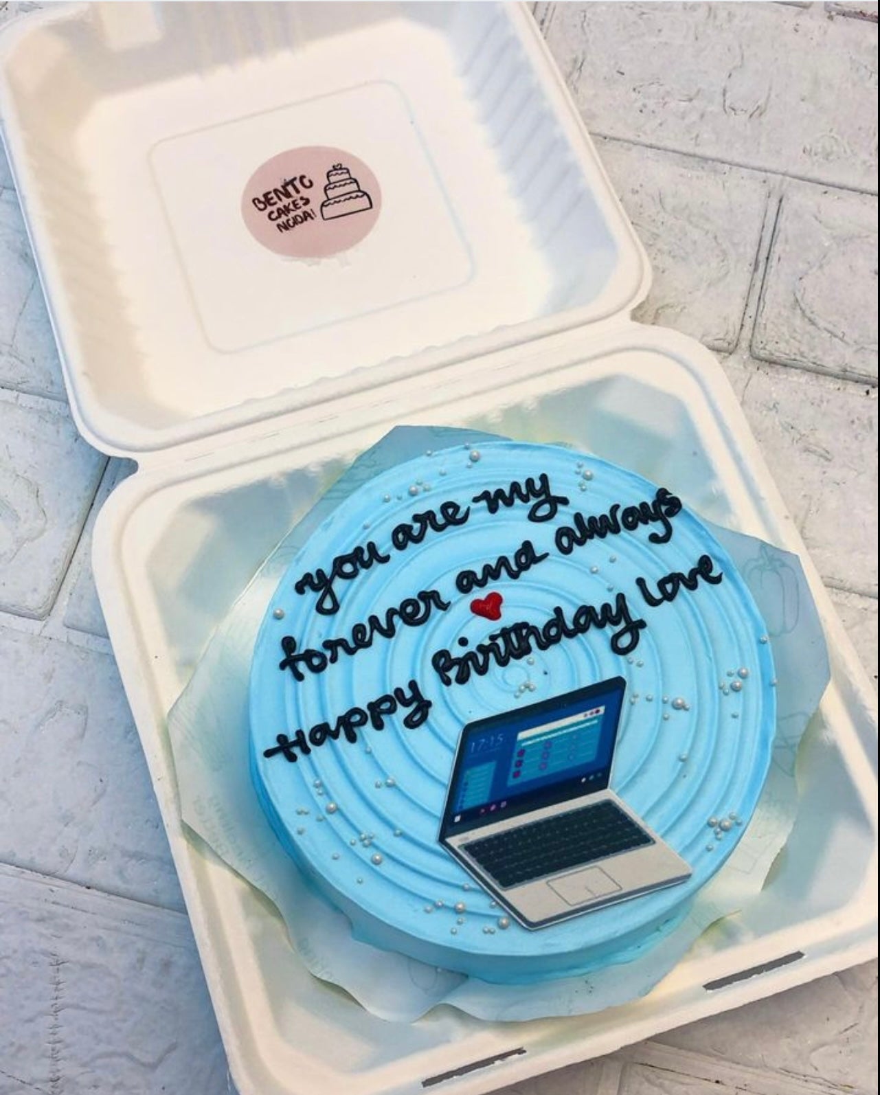 A light blue bento cake having a circular design on top with a laptop print for birthday.
