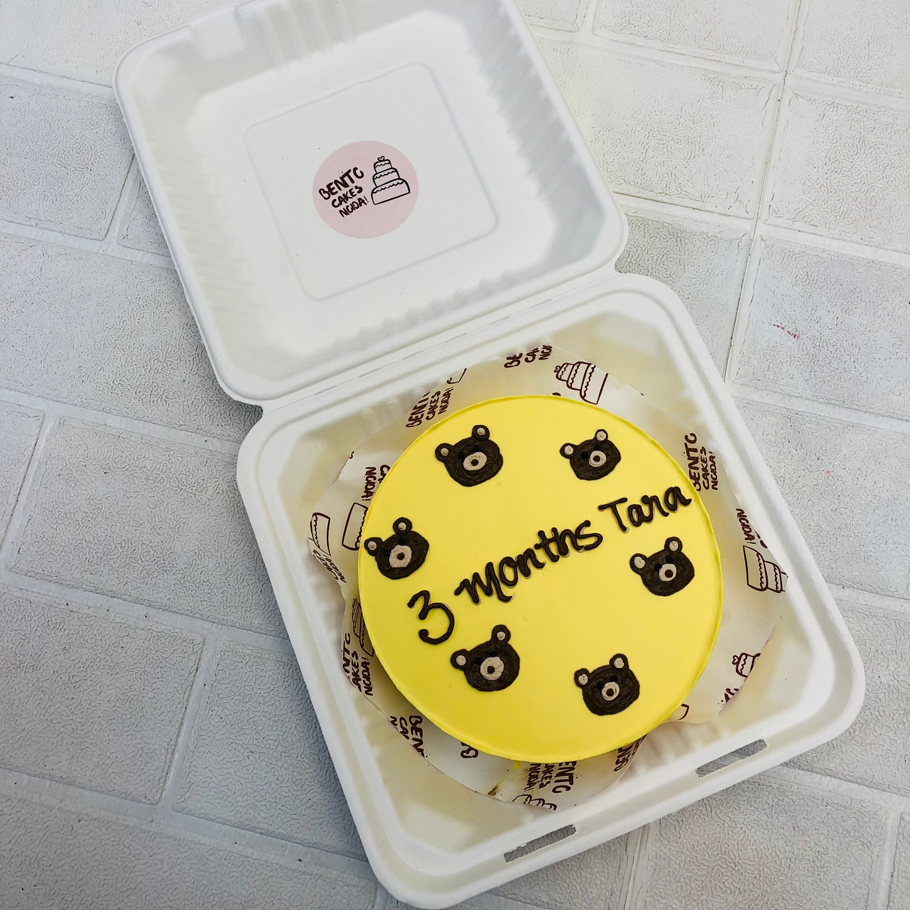A yellow bento cake with cute bear faces on it for 3 months baby.
