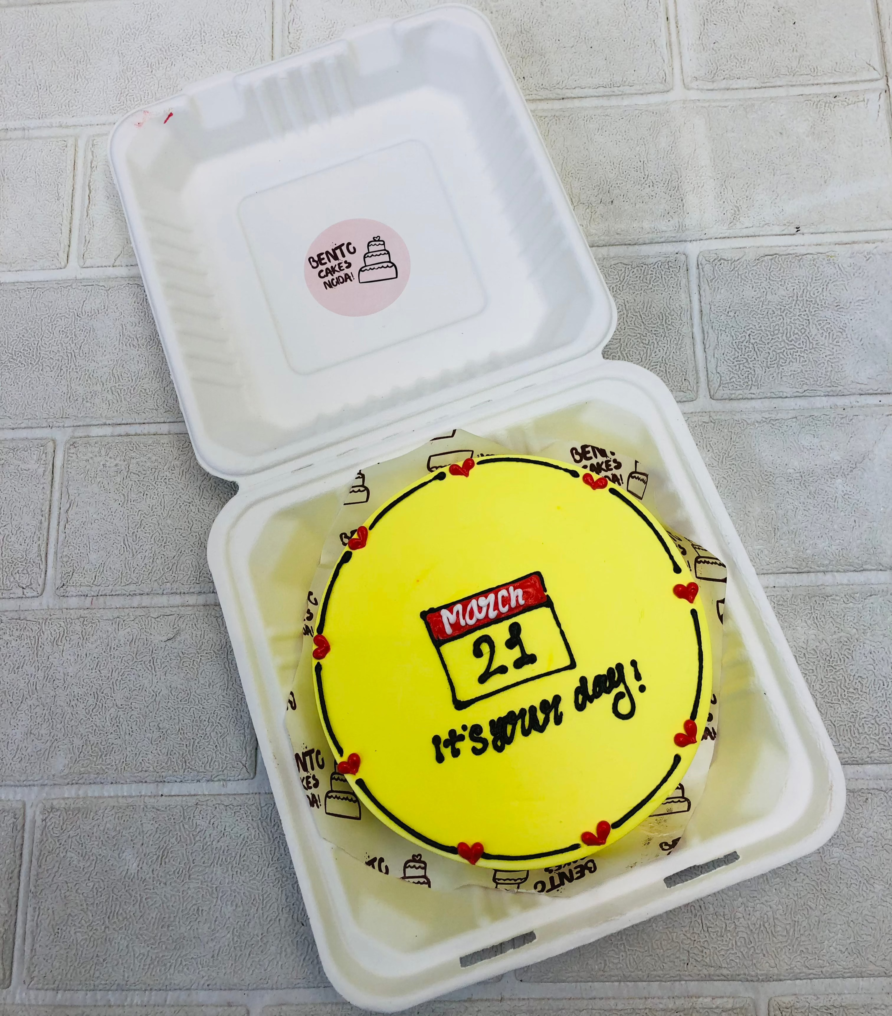 A yellow bento cake with calender date design on it.