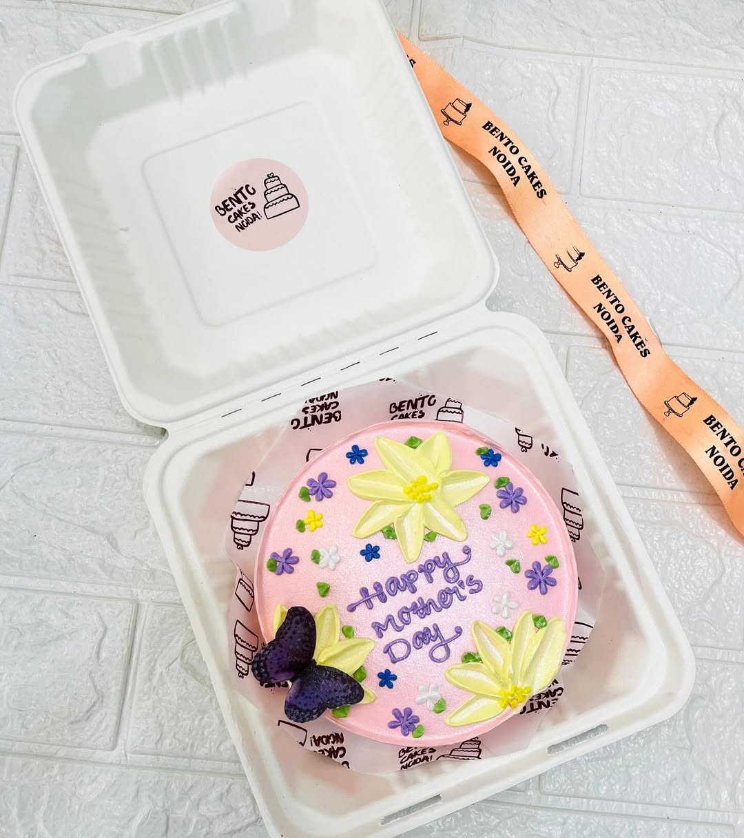 A light pink cake with yellow and purple floal design on it with a purple butterfly.