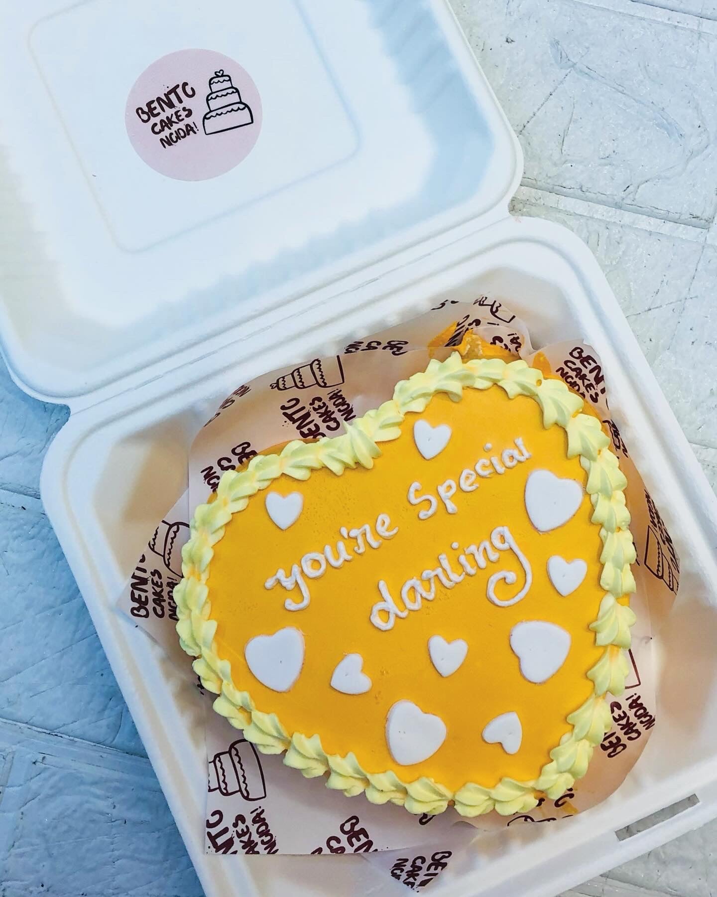 A yellow icing heart shape cake decorated with white fondant hearts and a text "you're special darling" written with white icing.
