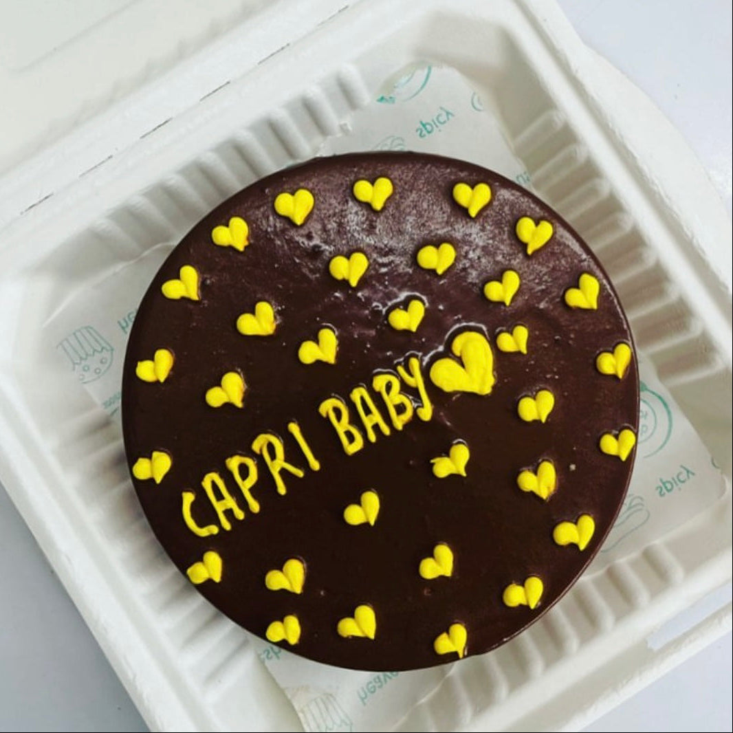 A chocolate cake featuring yellow heart decorations, displayed in a soft foam container.