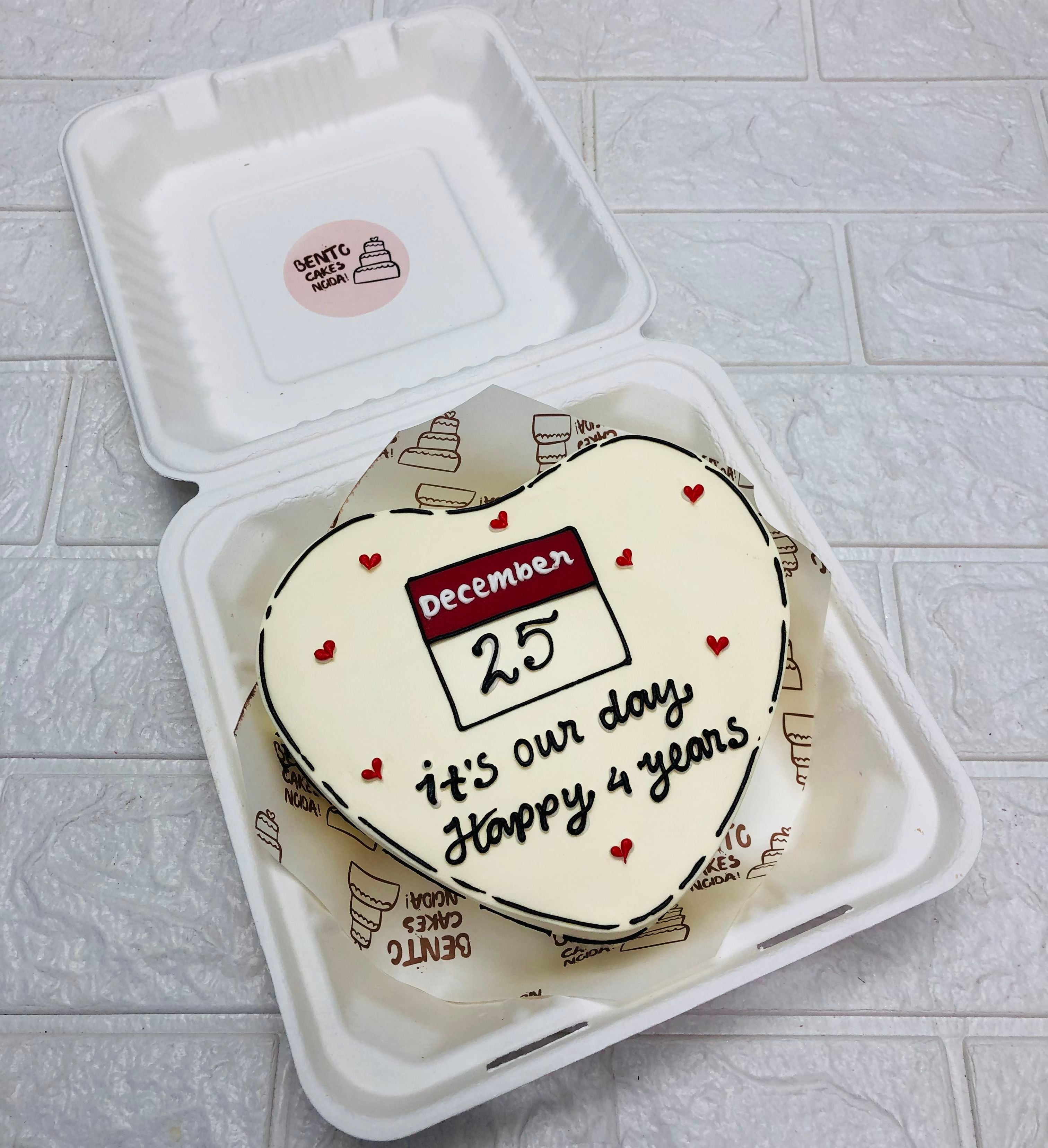 A offwhite heart shape cake designed with calender month and a beautiful text written with black icing on in.