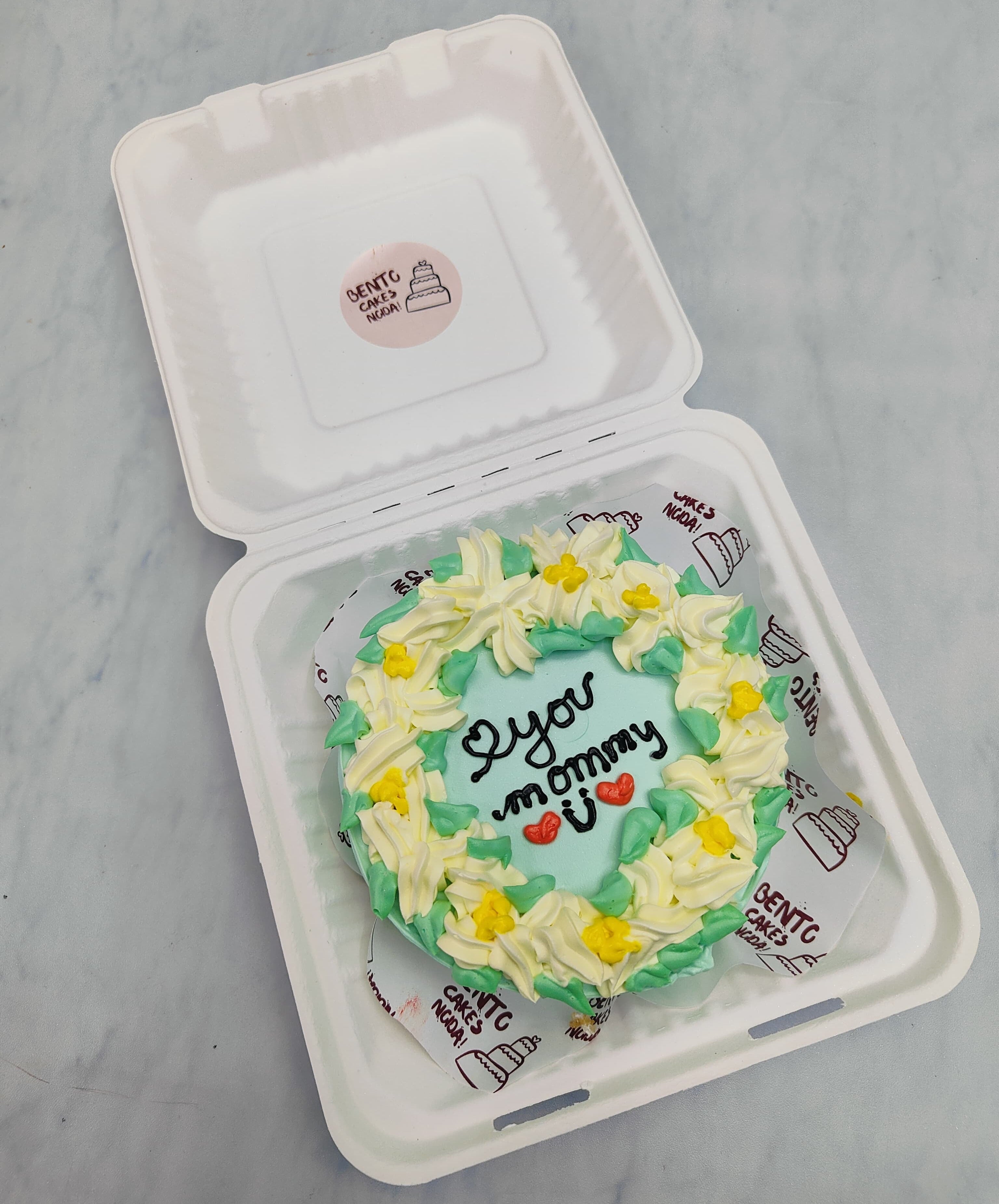 A light blue cake designed with colorful floral design and a text "love you mommy" on it.