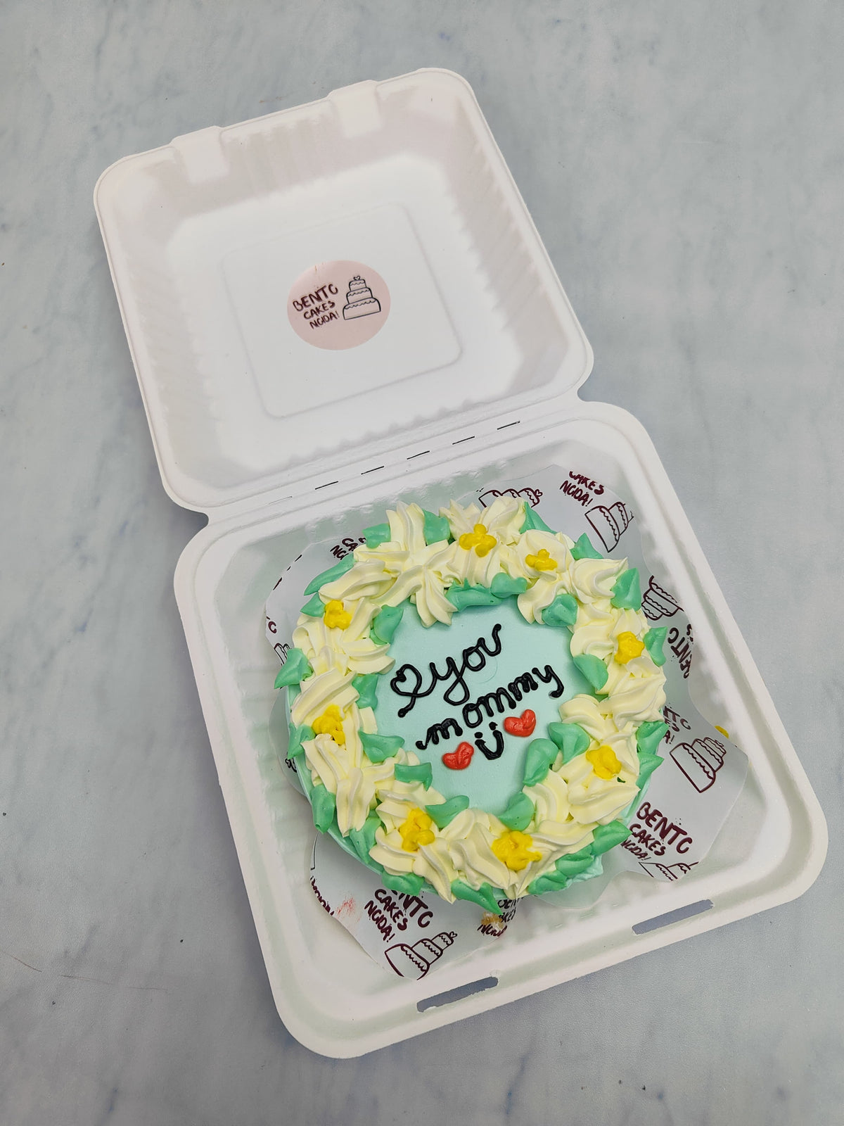 A light blue cake designed with colorful floral design and a text "love you mommy" on it.