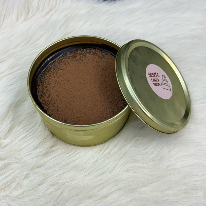 A luxurious Dream Tin Cake enclosed in an elegant golden tin, featuring a cracking chocolate disc, flowing chocolate liquid, luscious cream, and a soft, fluffy cake layer, displayed on a cozy white surface.